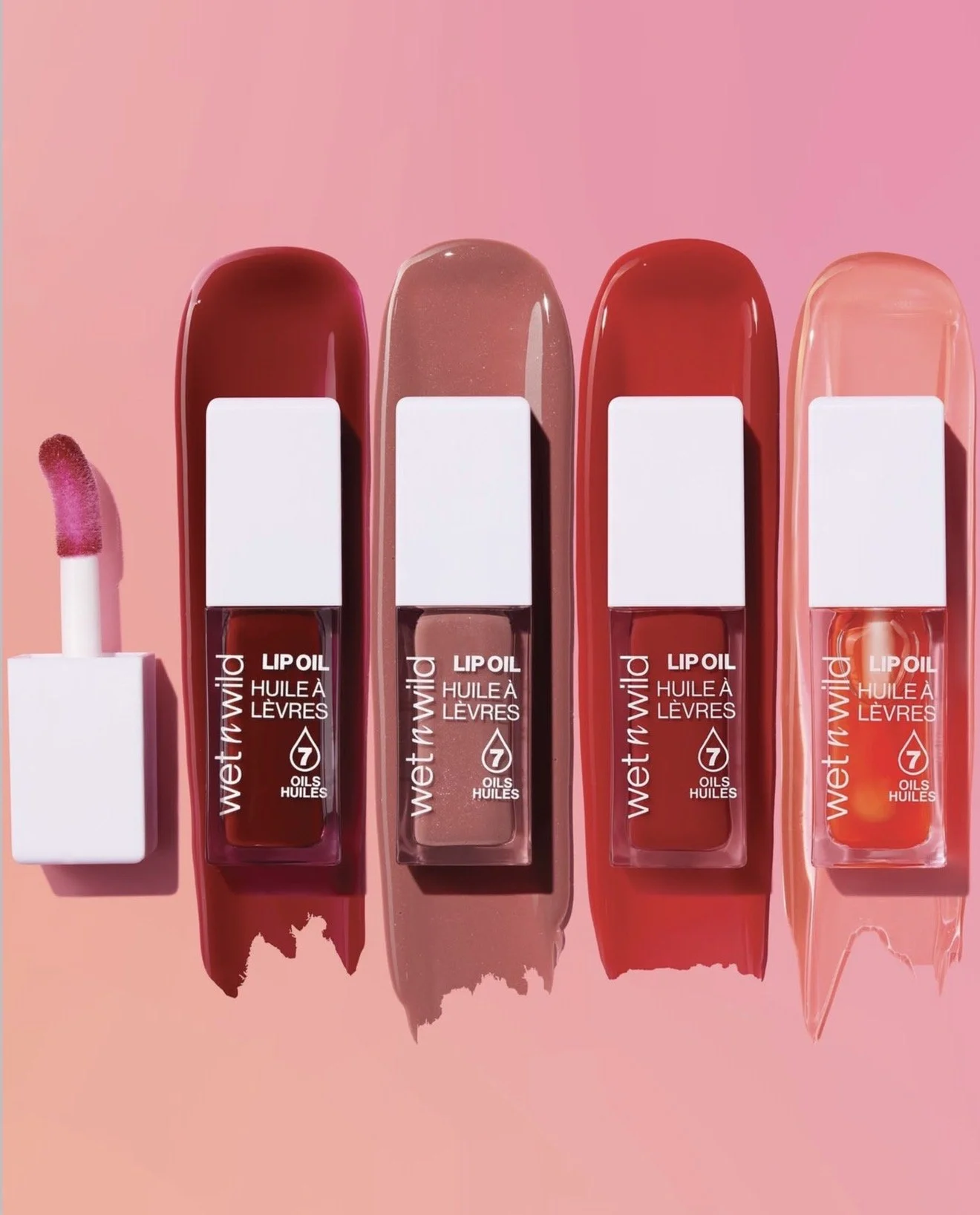 Four tubes of Wet n Wild lip oil in various shades with their caps removed, and an applicator wand with pink lip gloss on it. Product photography Los Angeles.