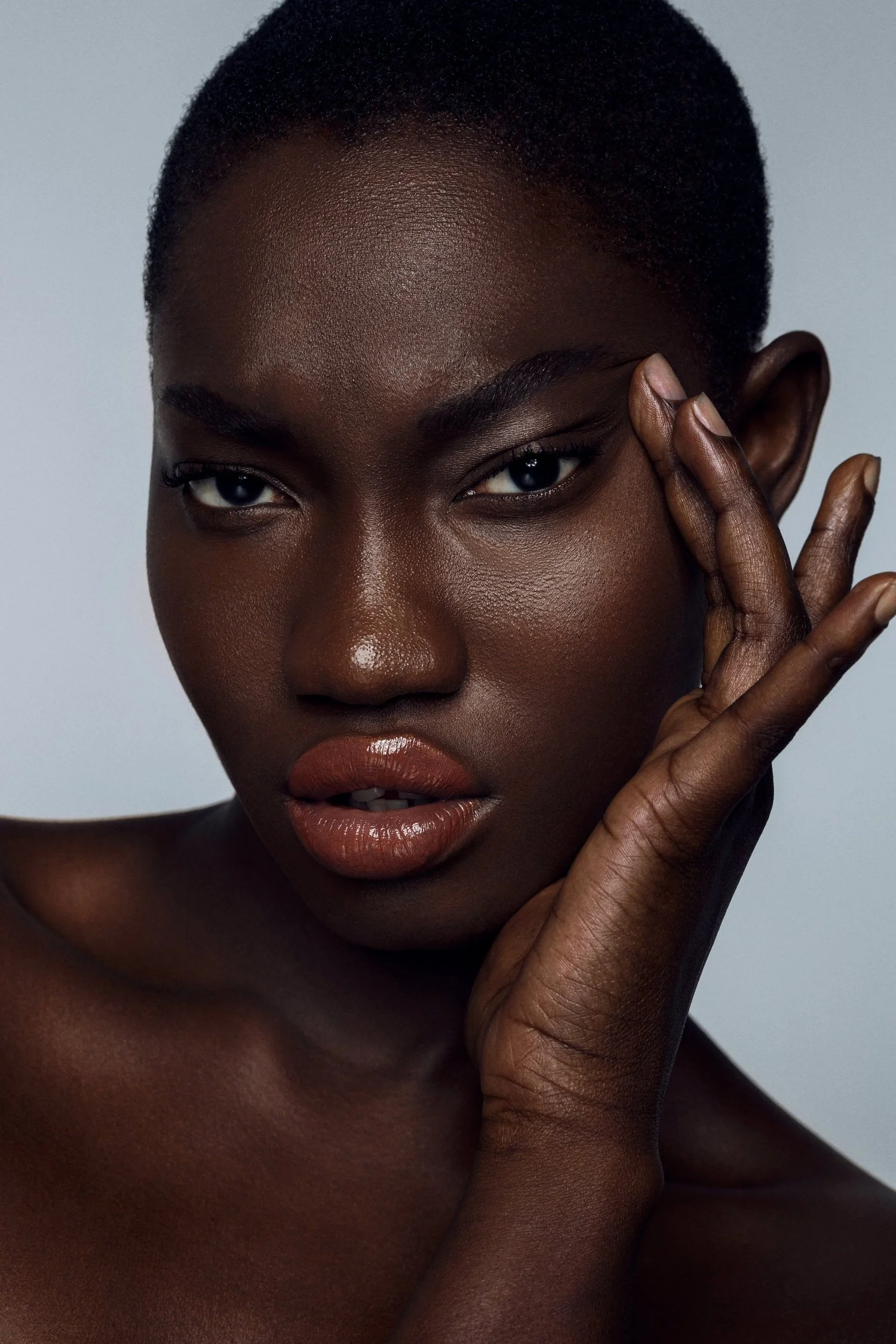 Close-up of a woman with dark skin, short hair, and natural makeup, touching her face with her right hand. Beauty Photographer Los Angeles.