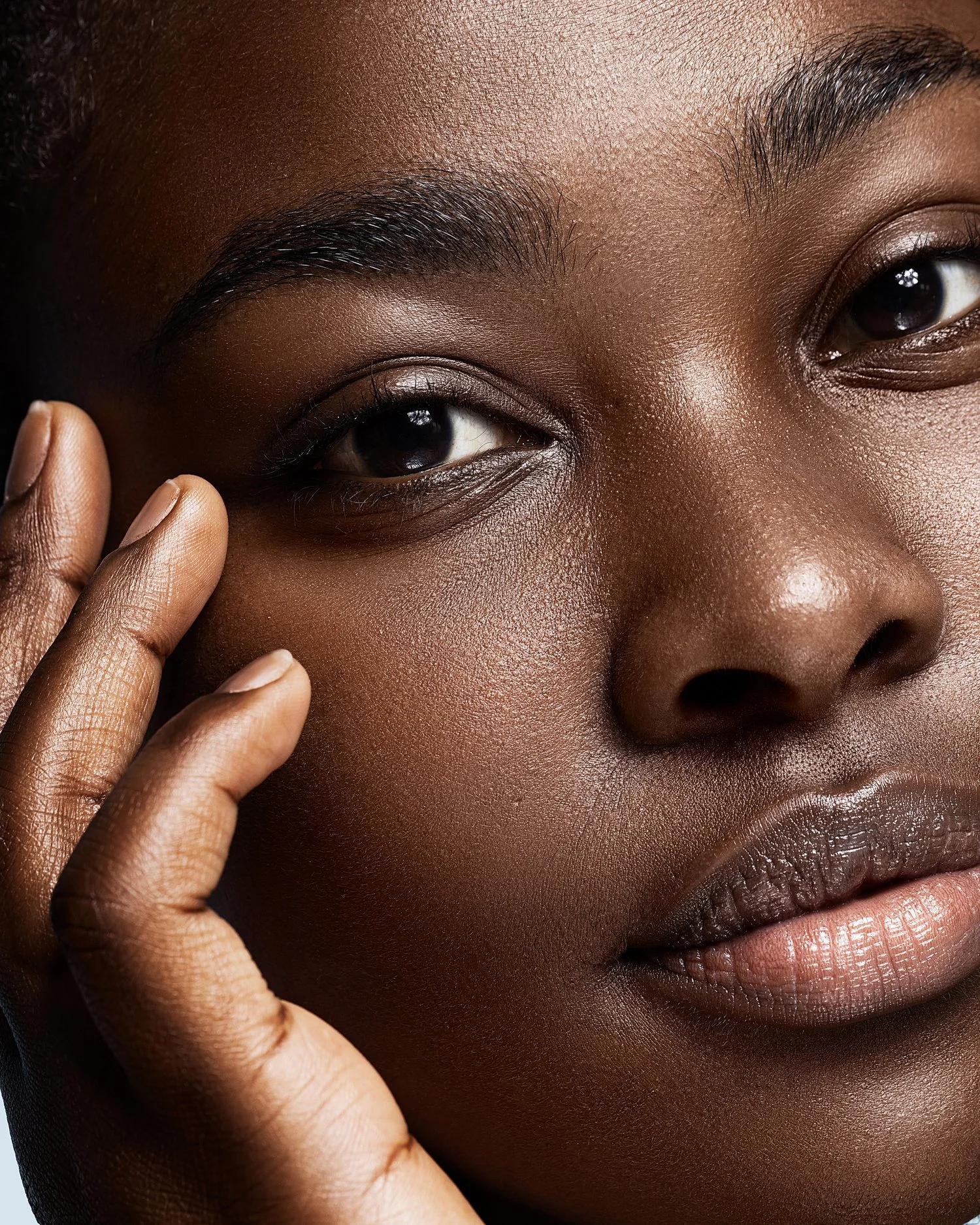 Close-up of a woman's face with dark skin, showing her eyes, nose, and lips, with one hand gently touching her face. Beauty Photographer Los Angeles.