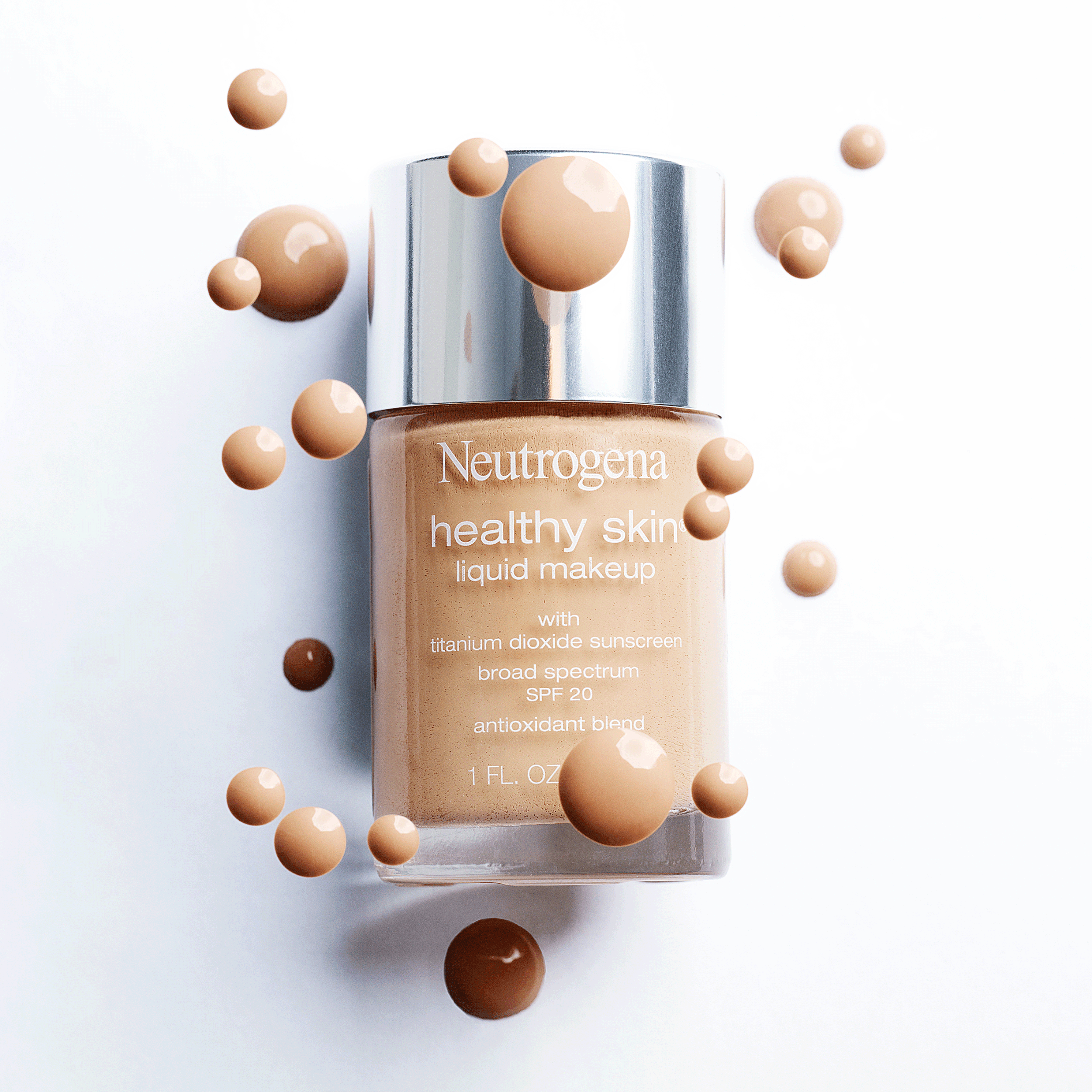 Bottle of Neutrogena healthy skin liquid makeup surrounded by various shades of beige and brown spherical drops. Product photography Los Angeles.