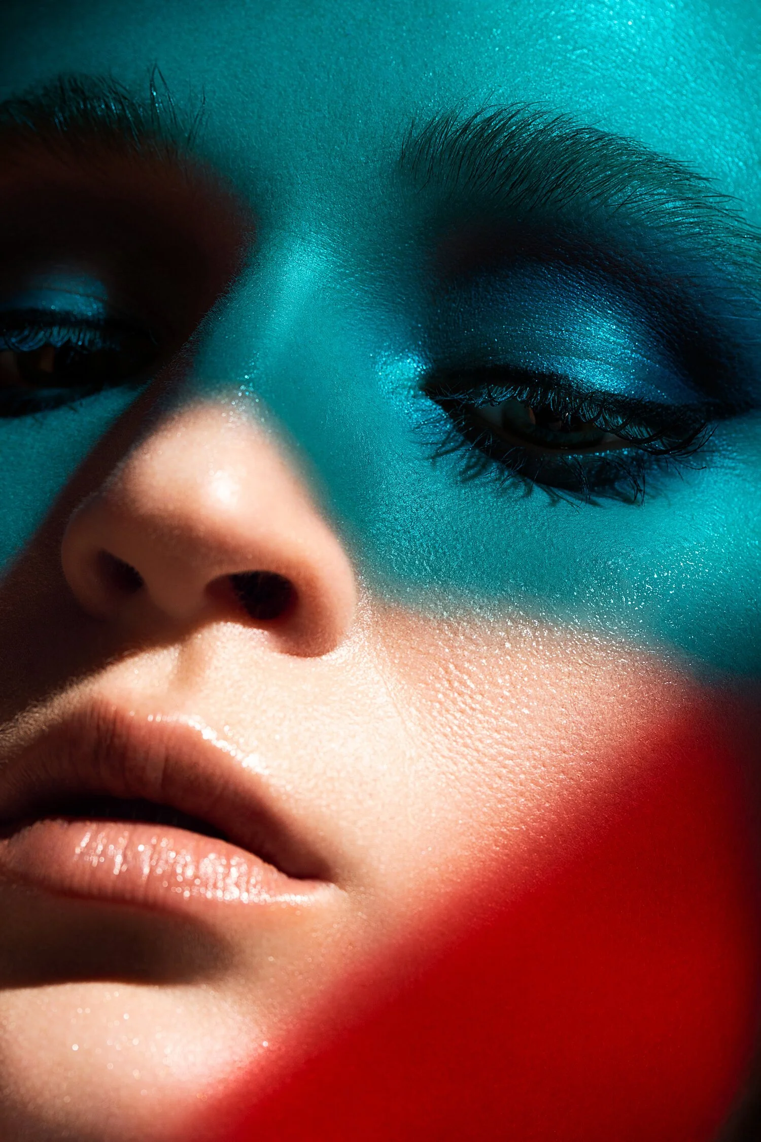 Close-up of a person's face with colorful makeup and dramatic lighting, focusing on the nose, lips, and partially closed eyes. Beauty Photographer Los Angeles.