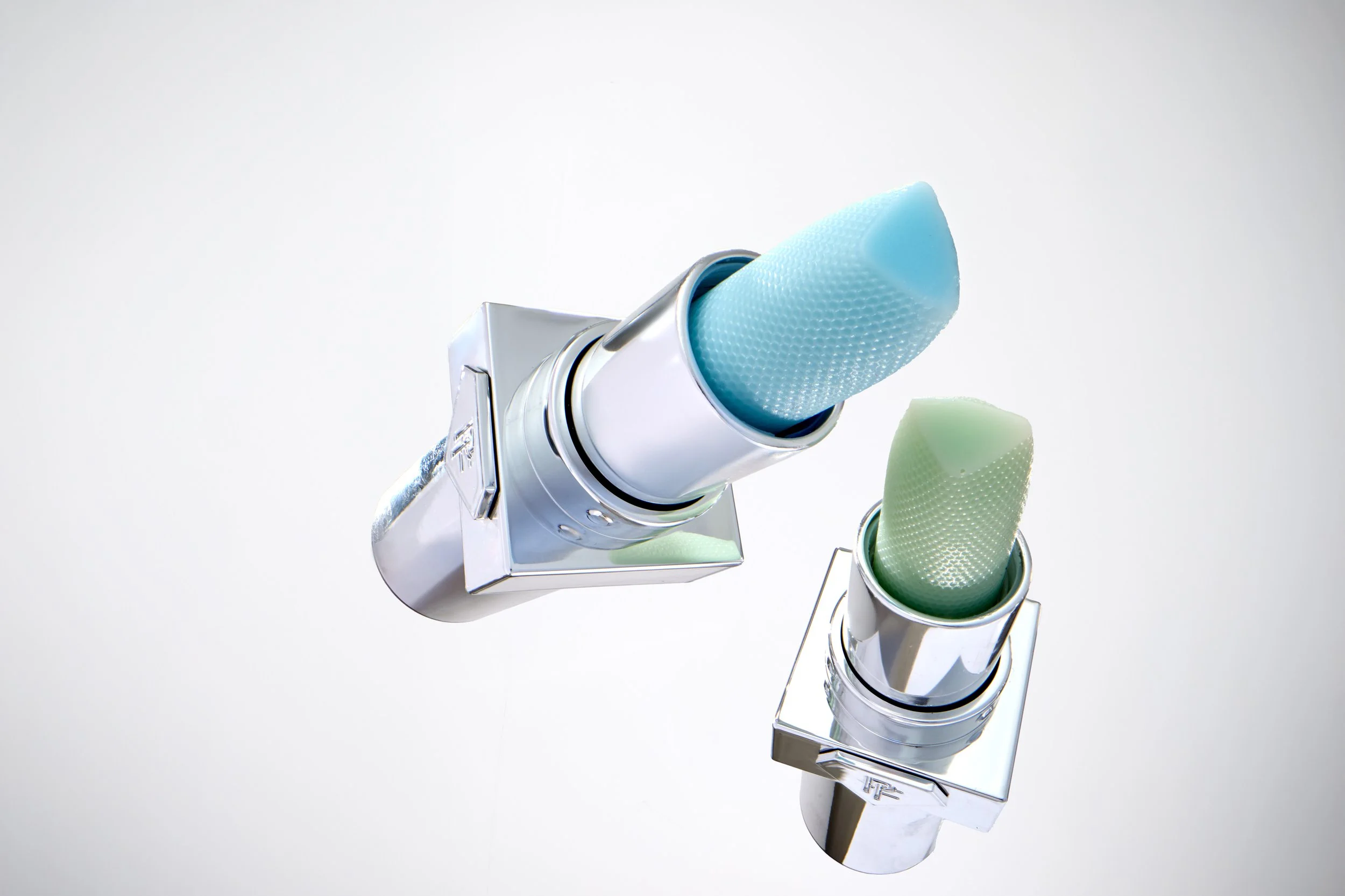 Close-up of two medical nasal spray bottles with transparent caps, one blue and one green, against a plain white background. Product photography Los Angeles.