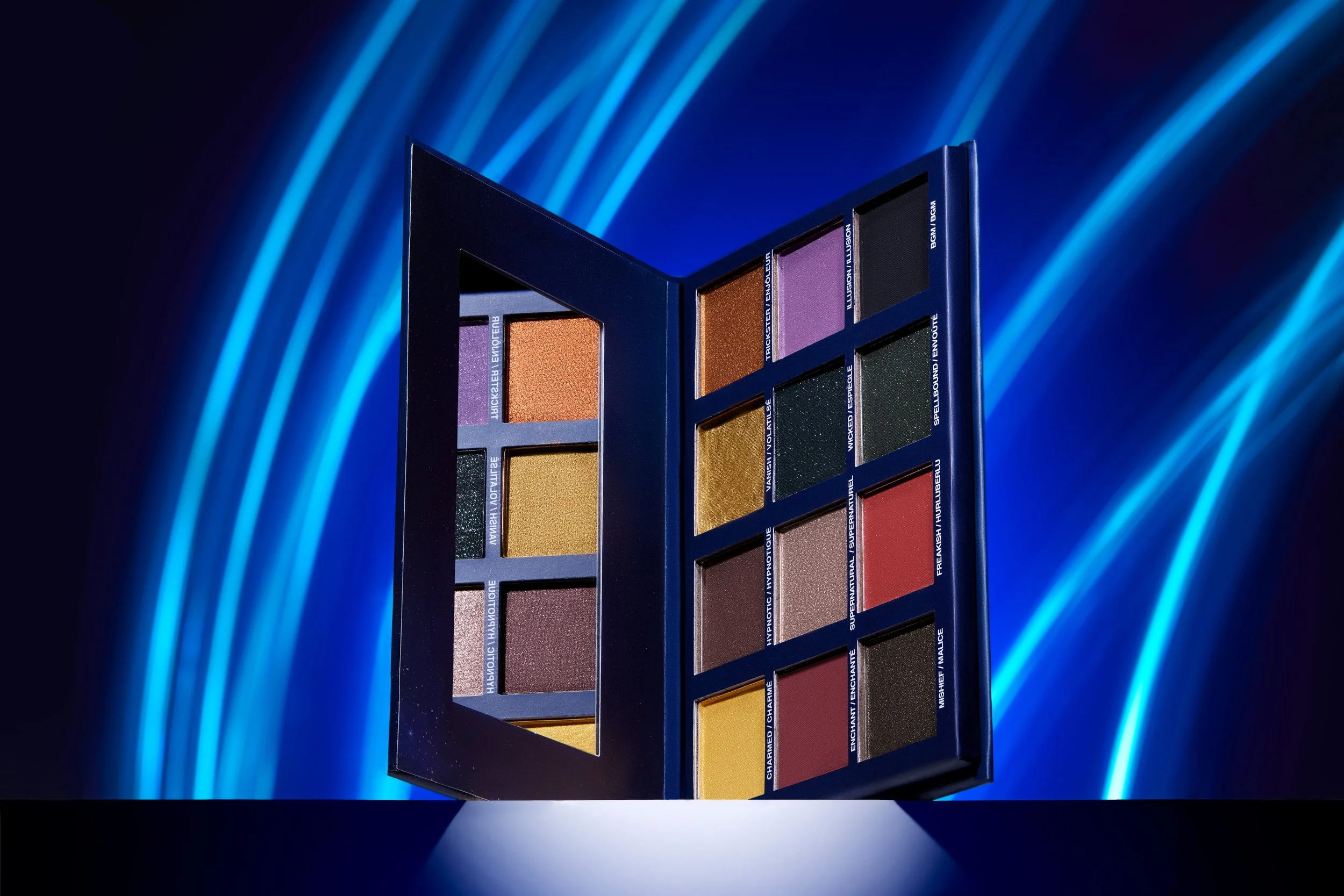 An open eyeshadow palette with twelve eyeshadow colors, displayed against a blue background with dynamic light streaks. Product photography Los Angeles.