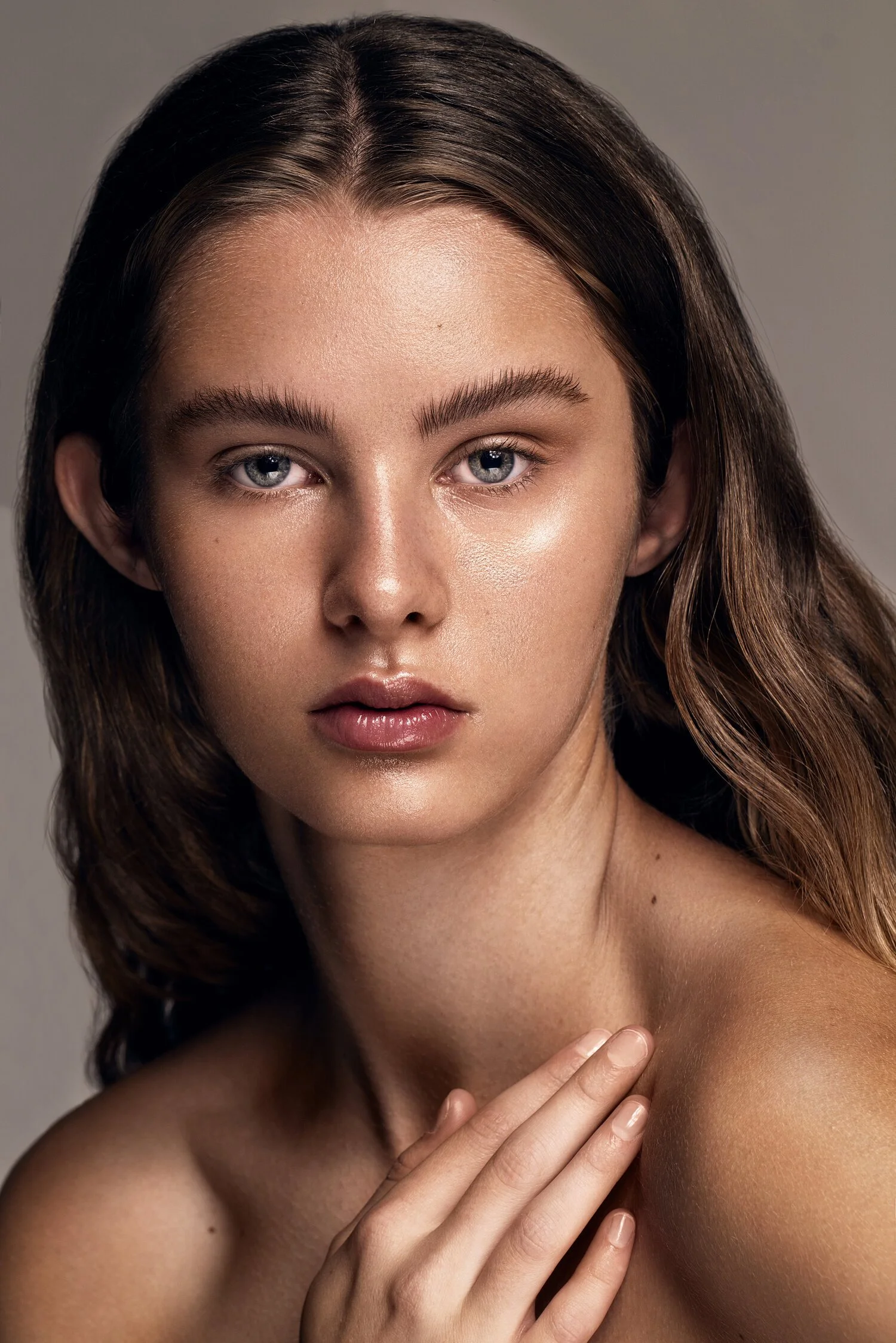 Close-up portrait of a young woman with long brown hair, blue eyes, and natural makeup, touching her shoulder with her hand. Beauty Photographer Los Angeles.