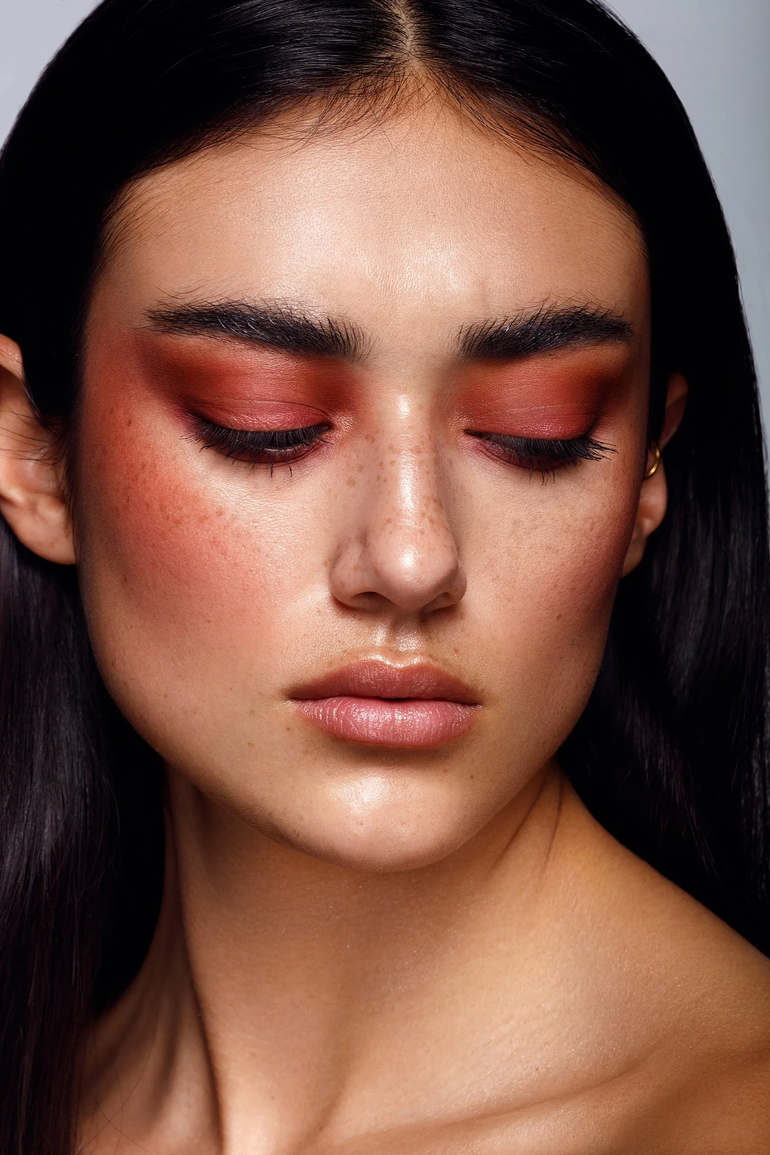 Close-up of a woman with closed eyes, dark hair, and natural makeup including red eyeshadow, mascara, and light lipstick. Beauty Photographer Los Angeles.