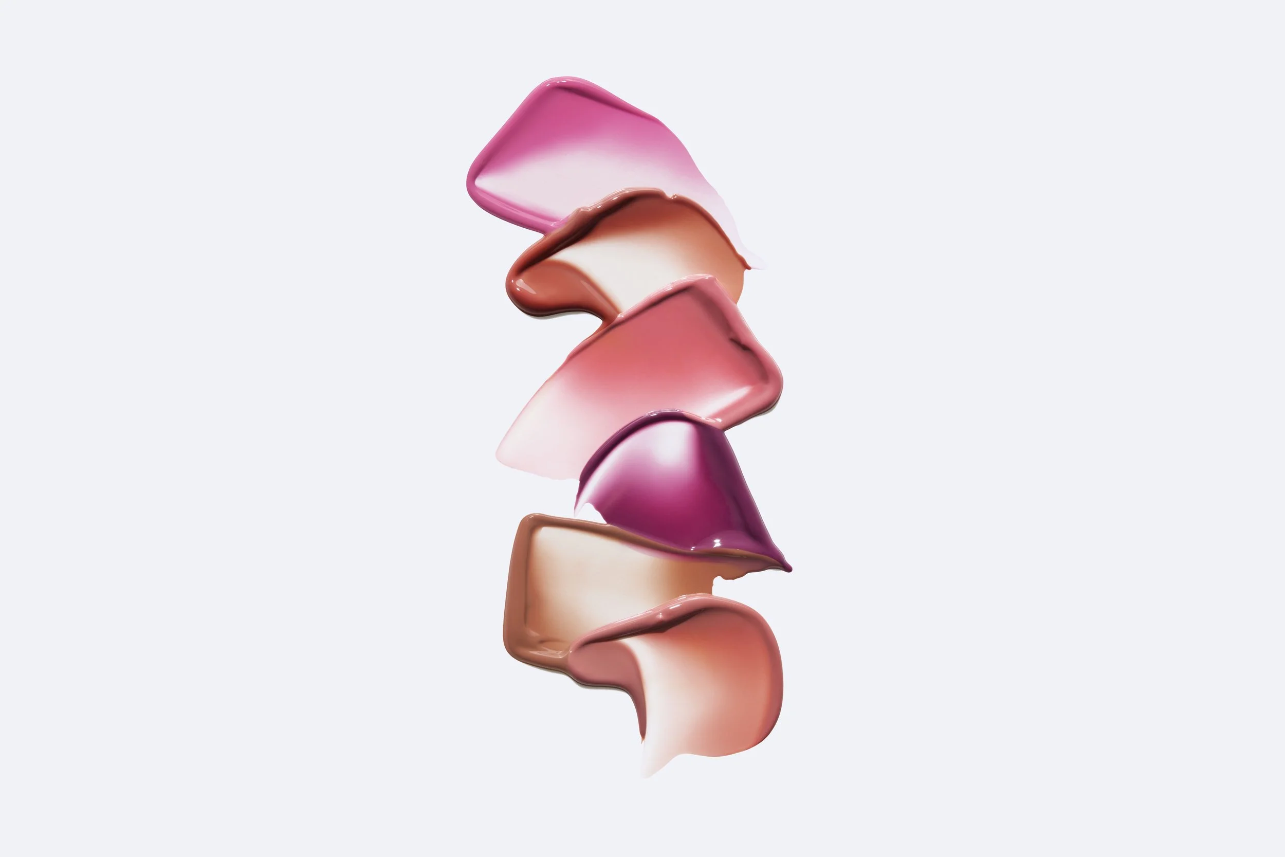 Multiple swatches of pink, red, peach, and purple lipstick or makeup cream arranged vertically on a light background. Product photography Los Angeles.