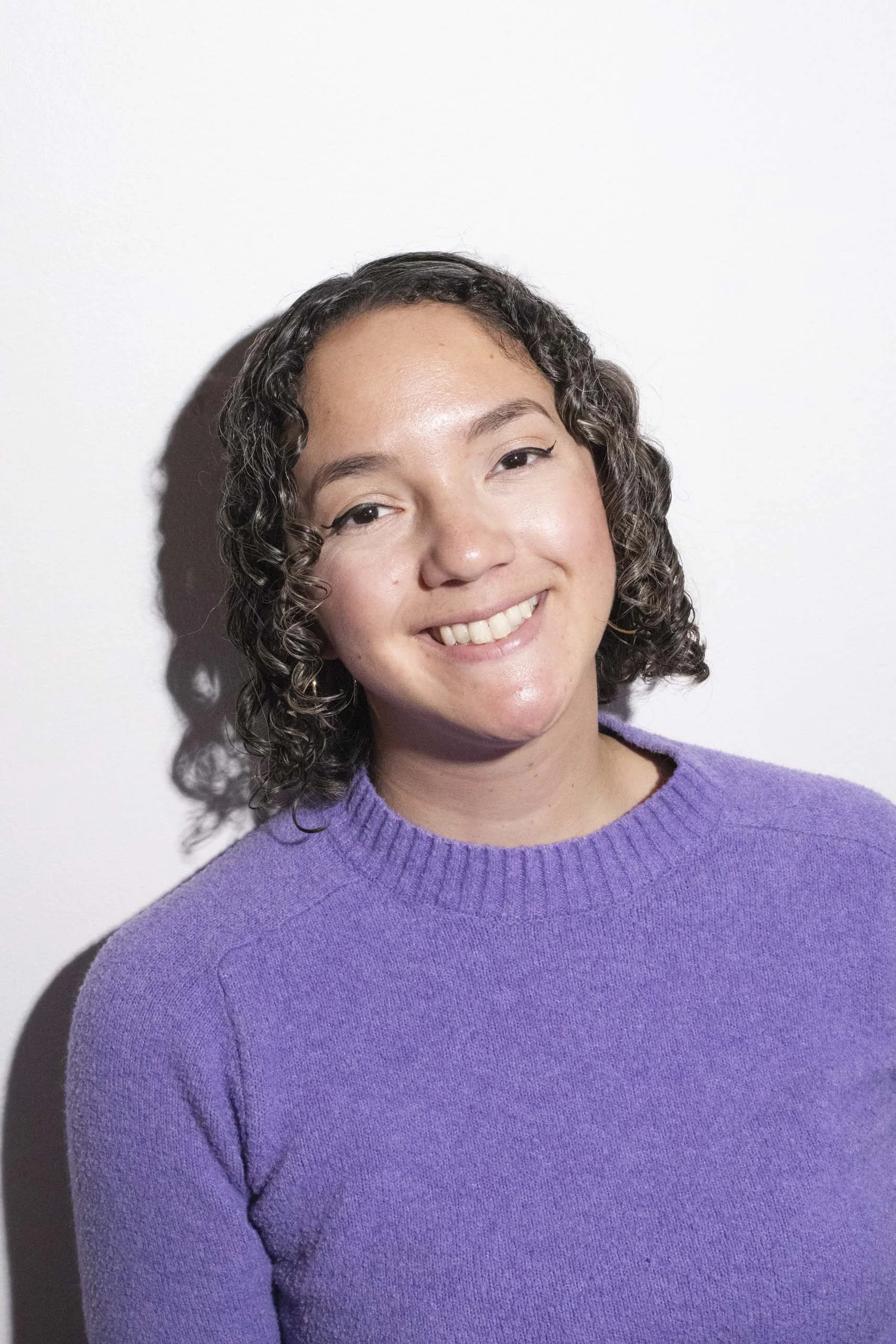Evelyn Sisk smiles wearing a purple sweater in front of a white wall