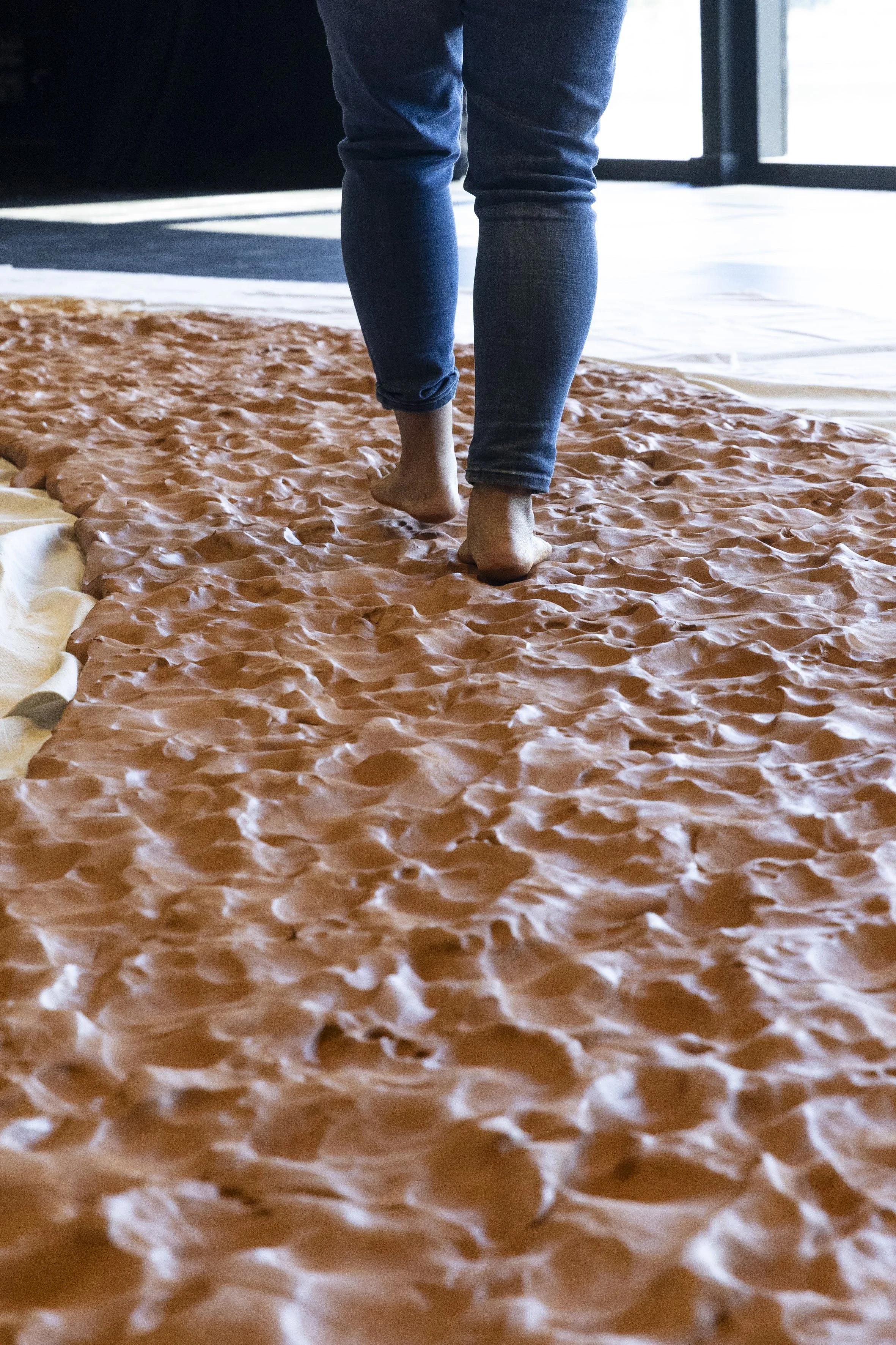 Person walking barefoot on a textured clay participating in community created artwork