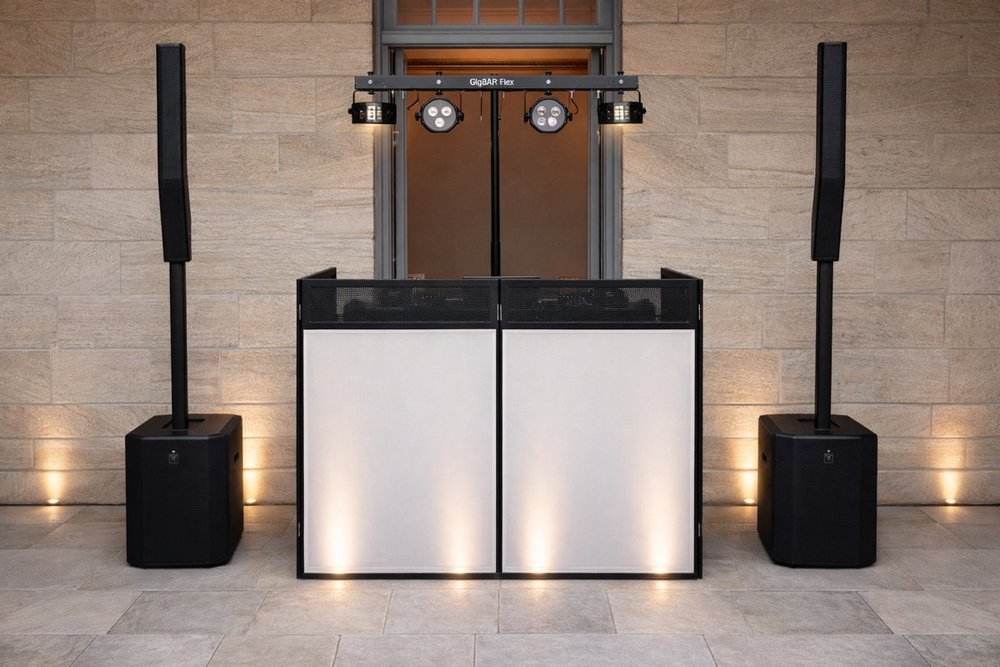 The Bass Drop wedding DJ setup with white DJ booth, column speakers and GigBar Flex lighting