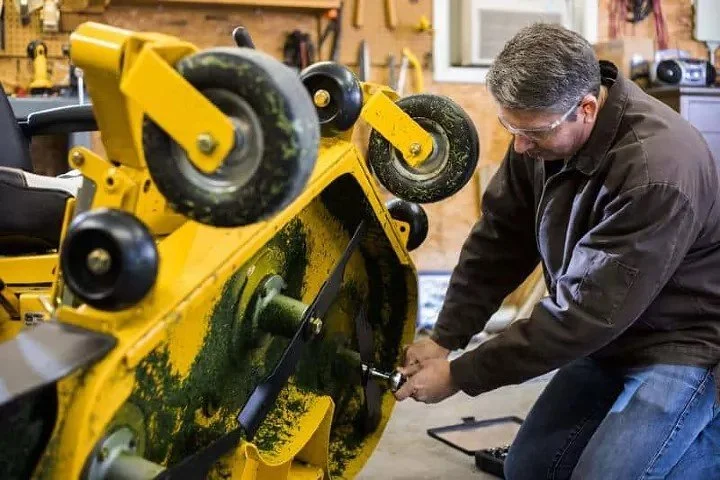 A man working on a yellow riding lawn mower in a garage workshop.
