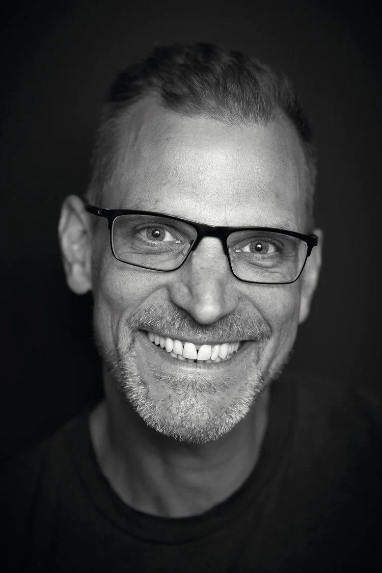 Black and white close-up portrait of a smiling man with glasses, short hair, and a beard.