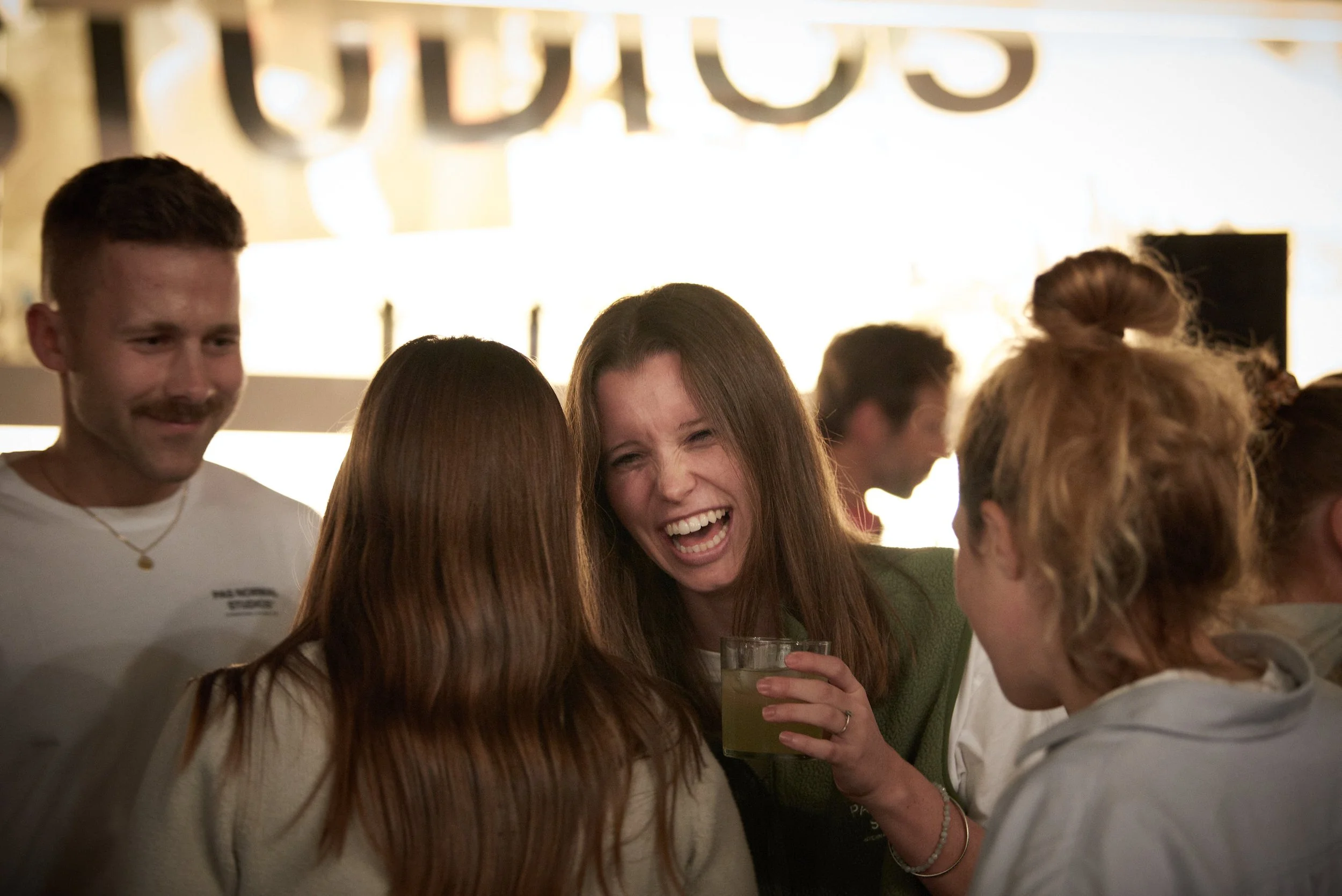 Group of people socializing and having fun at a bar or restaurant, with smiling and laughing women holding drinks.