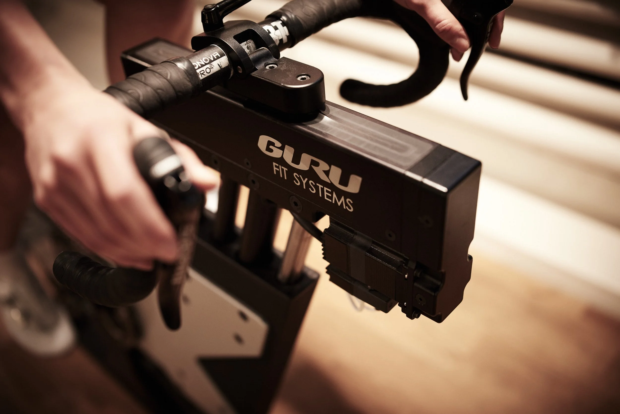 Close-up of a person holding a GURU Fit Systems bike trainer on a bike.