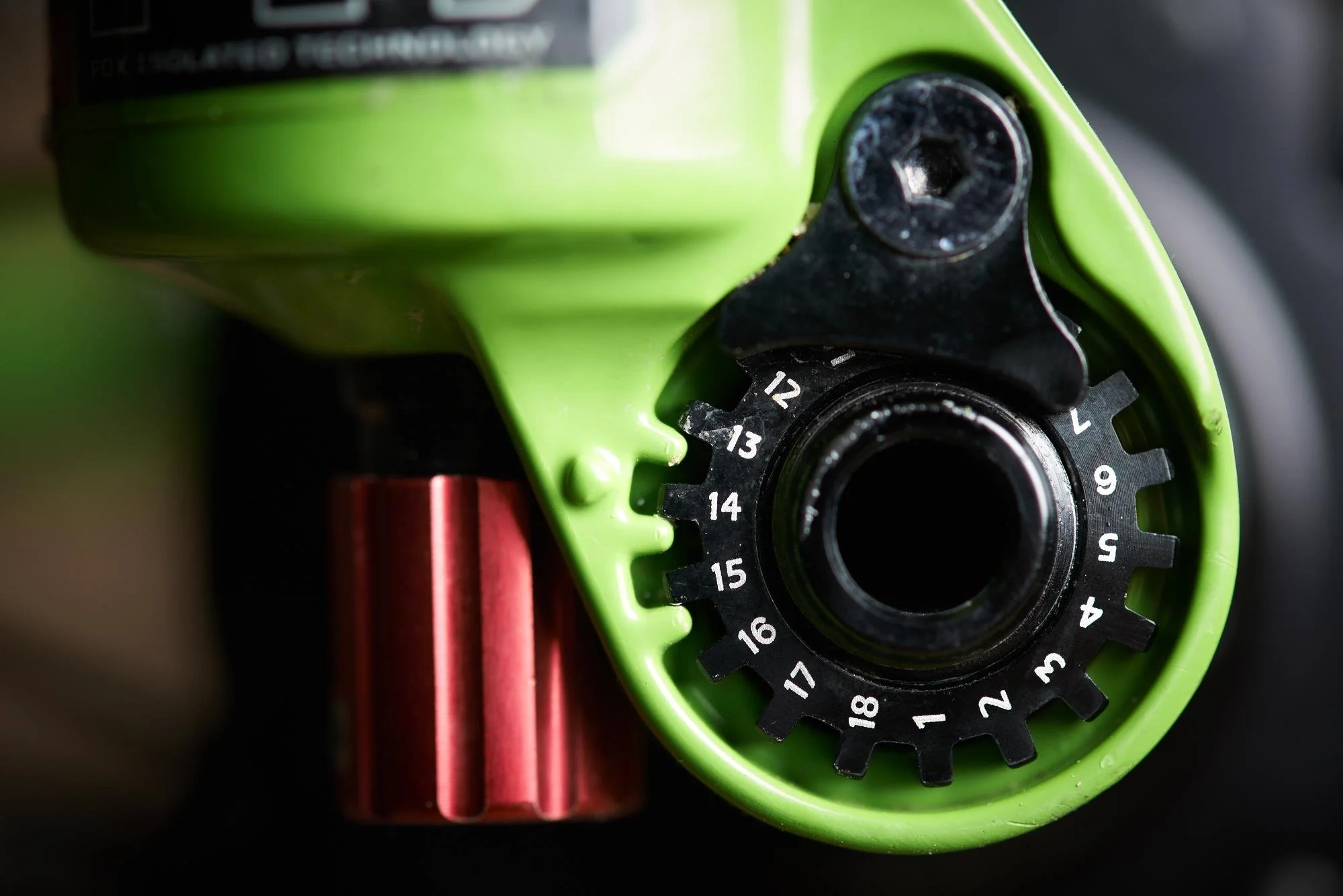 Close-up of a bicycle gear system, showing a black gear dial with numbered settings from 1 to 18, attached to a green frame with a red component nearby.