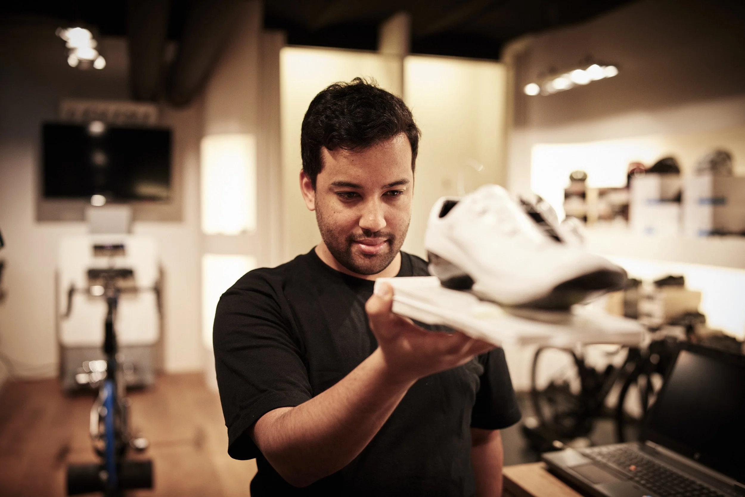 A man examining a white and black sports shoe and a stack of papers in a store or workshop.