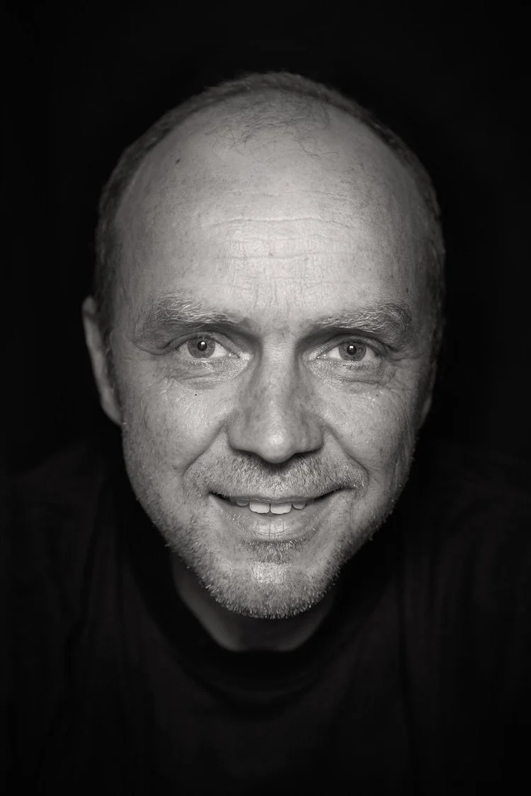 Black and white portrait of a smiling middle-aged man with short hair and light stubble, looking directly at the camera.