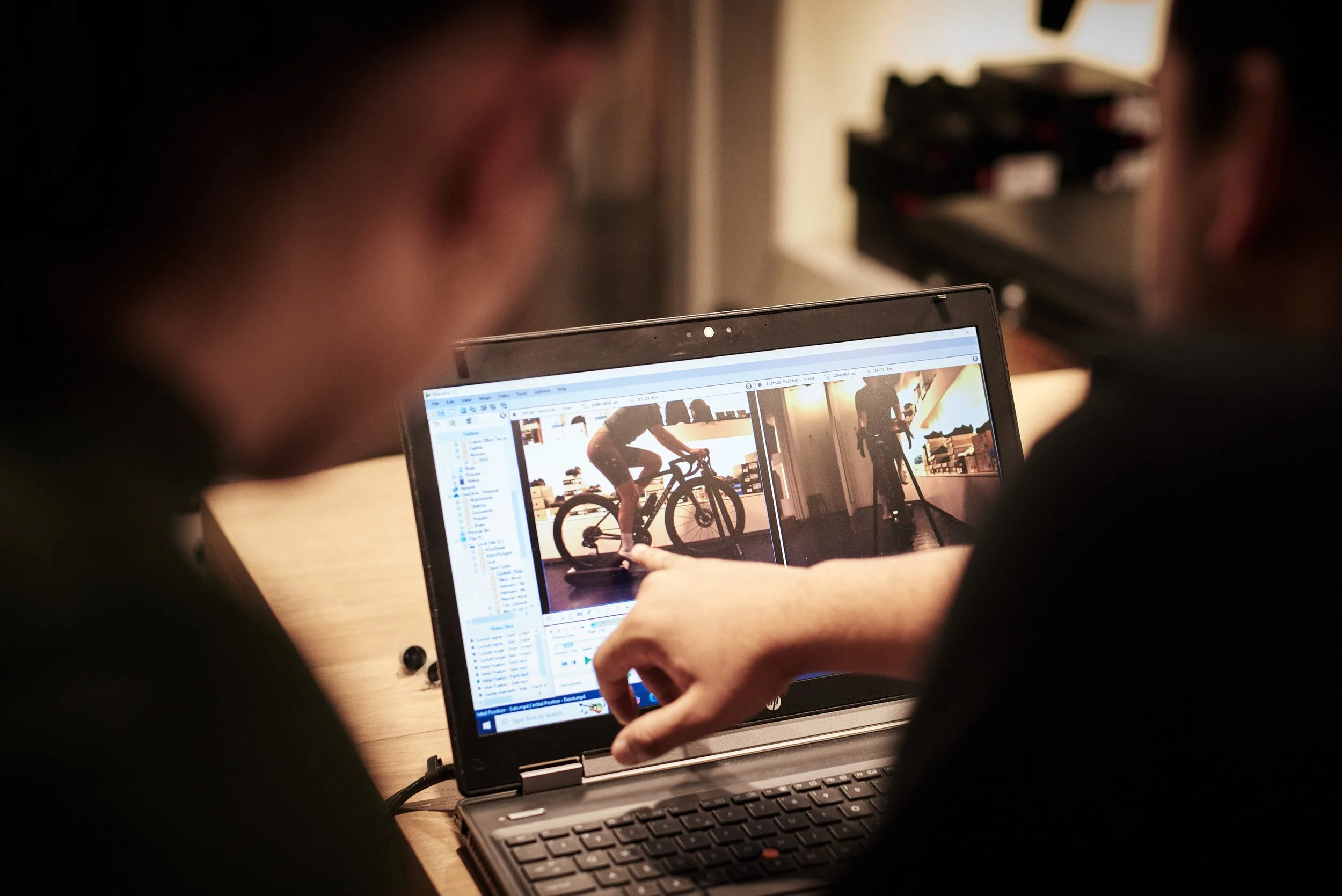 Two people working on a laptop editing photos of a person on a bike, indoor setting.