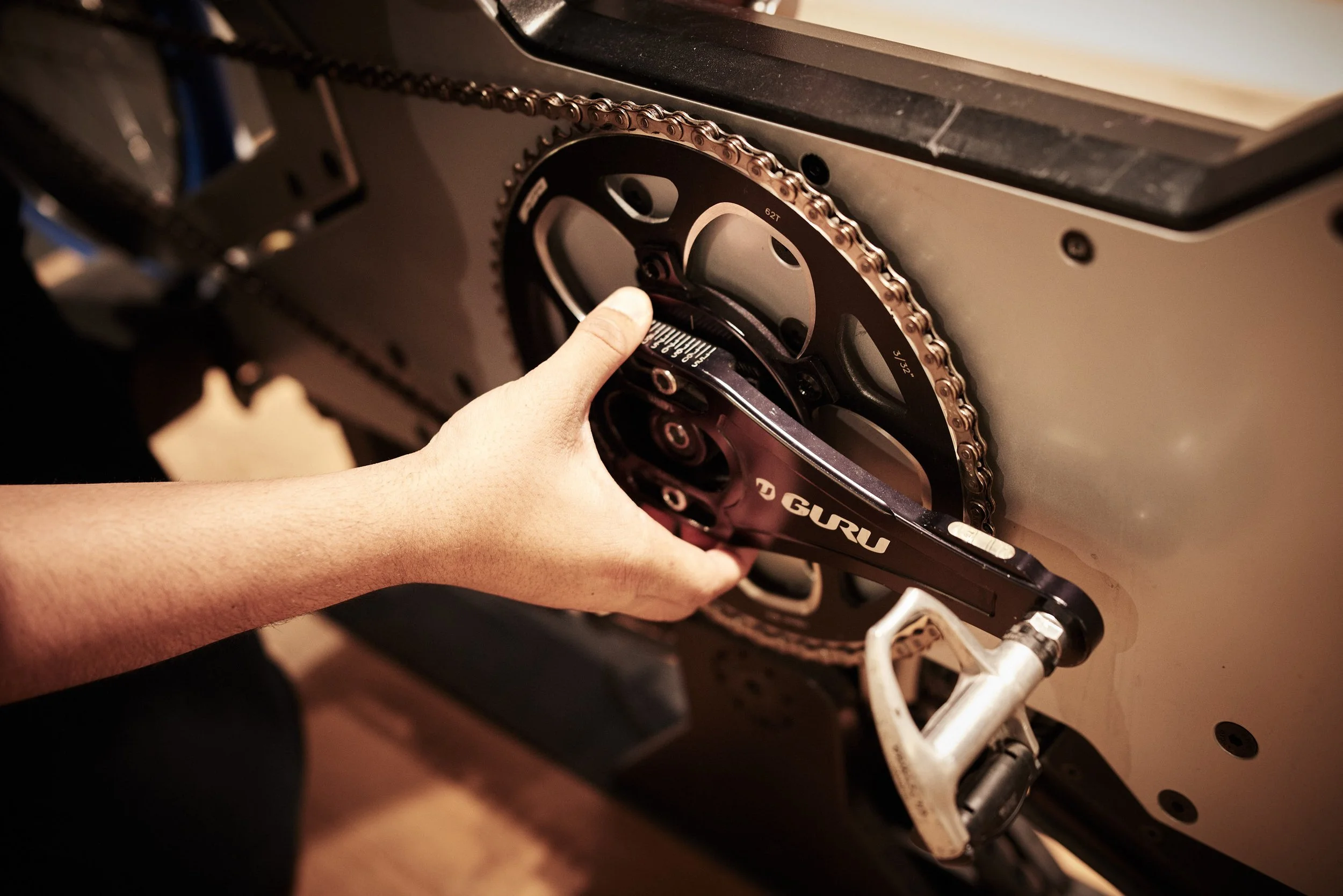 Person installing a GURU crankset onto a bicycle's bottom bracket with tools.