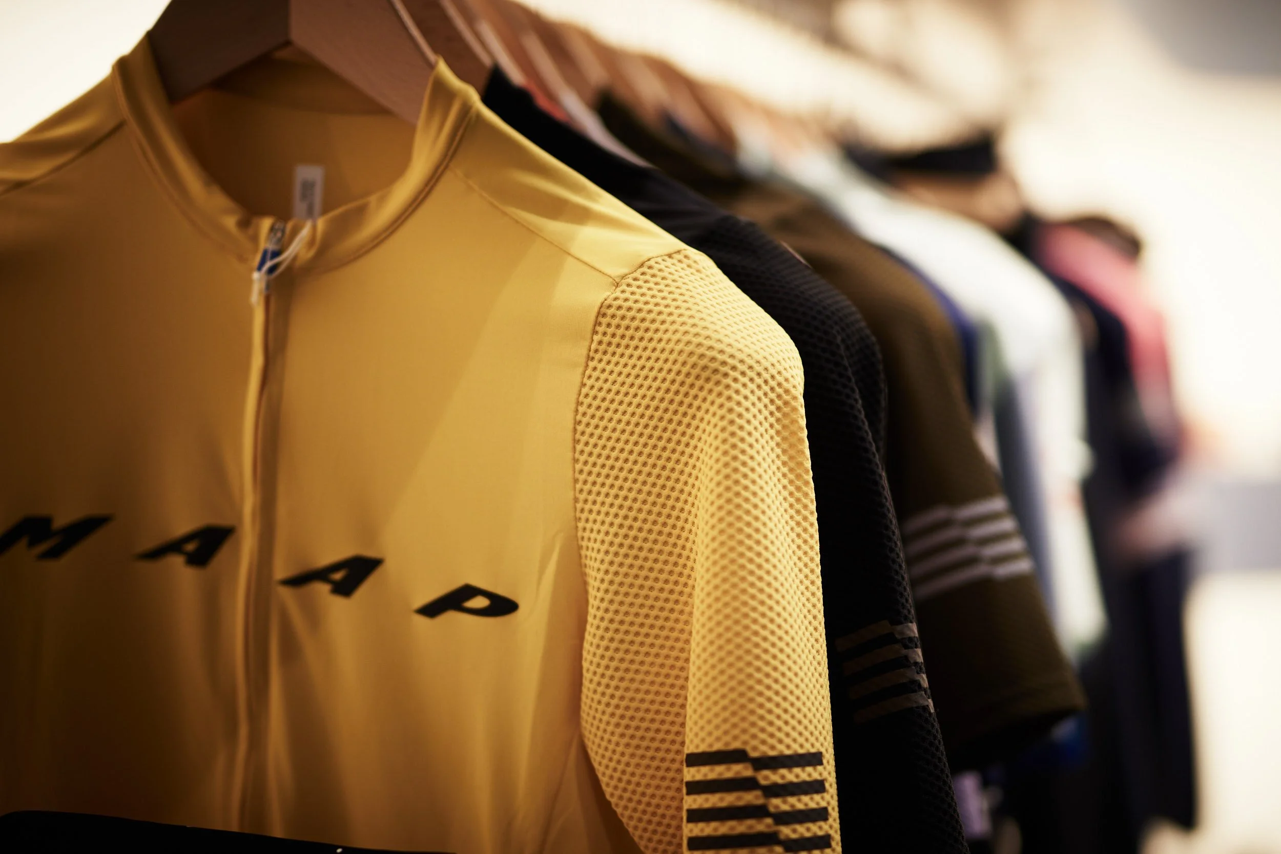 A yellow sports jersey hanging on a rack among other multicolored jerseys.