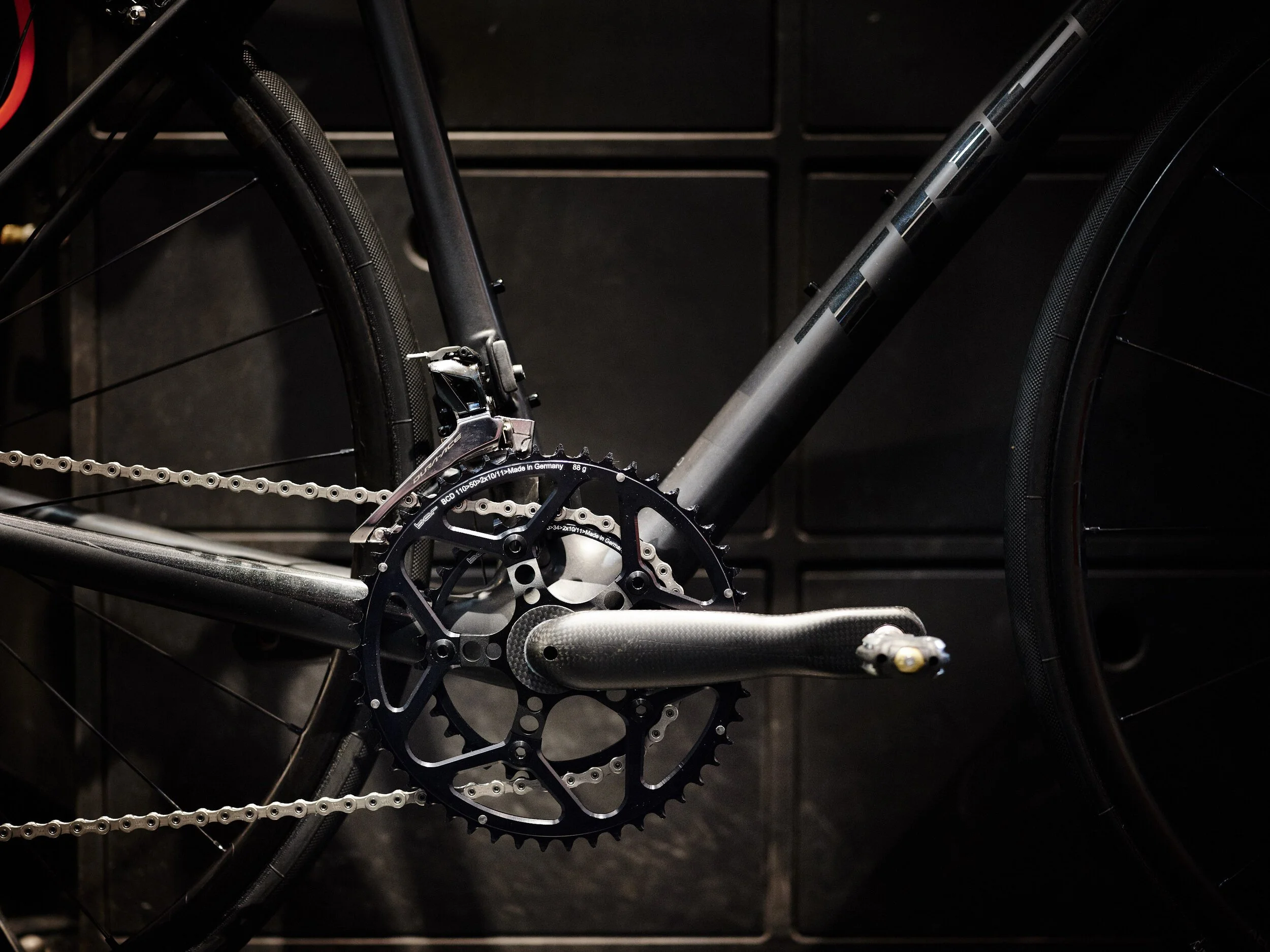 Close-up view of a black bicycle's chainring and crankset with a black frame, black tires, and a black background.