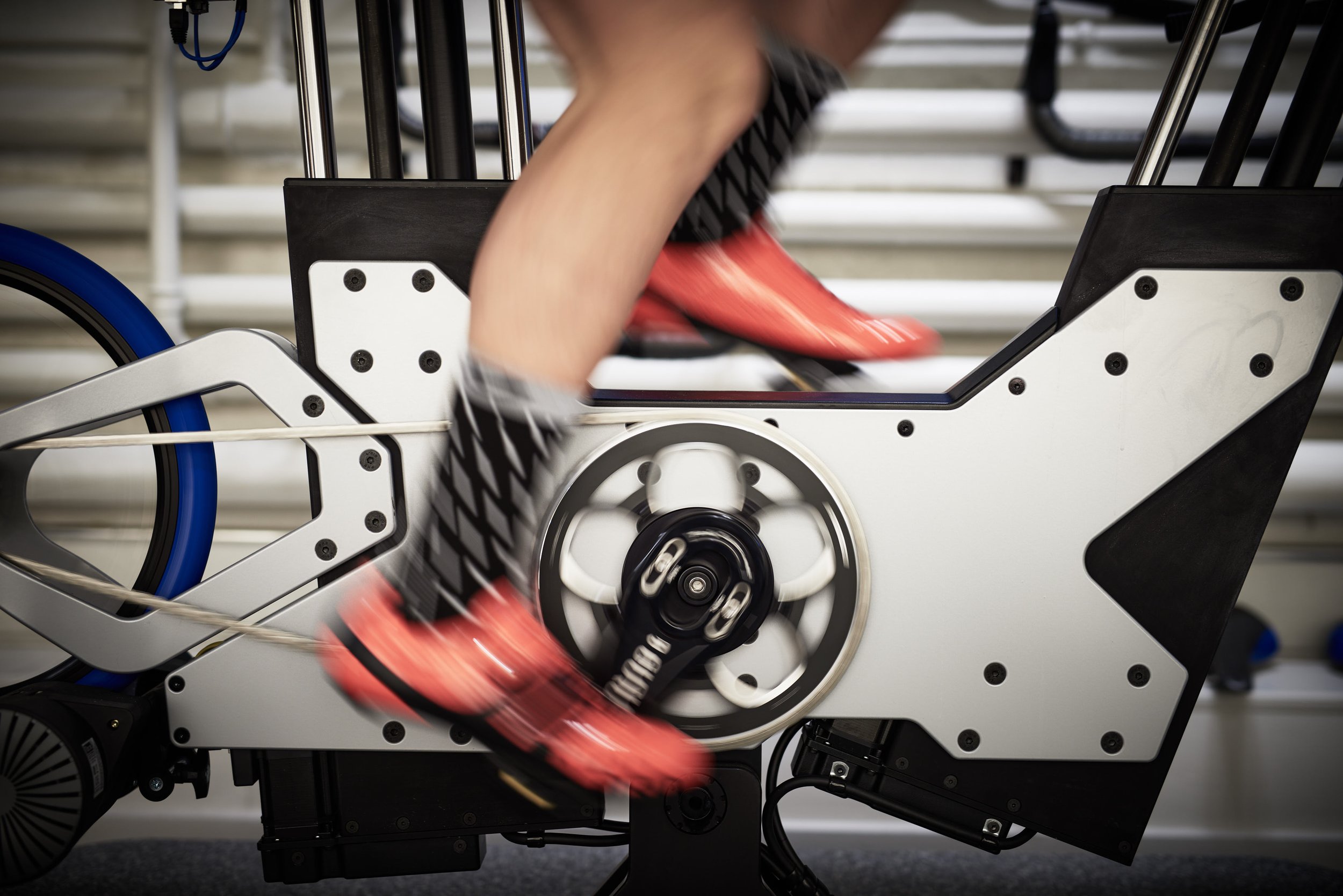 Close-up of a person riding a stationary exercise bike, focusing on the pedals and lower body, with a blurred background.