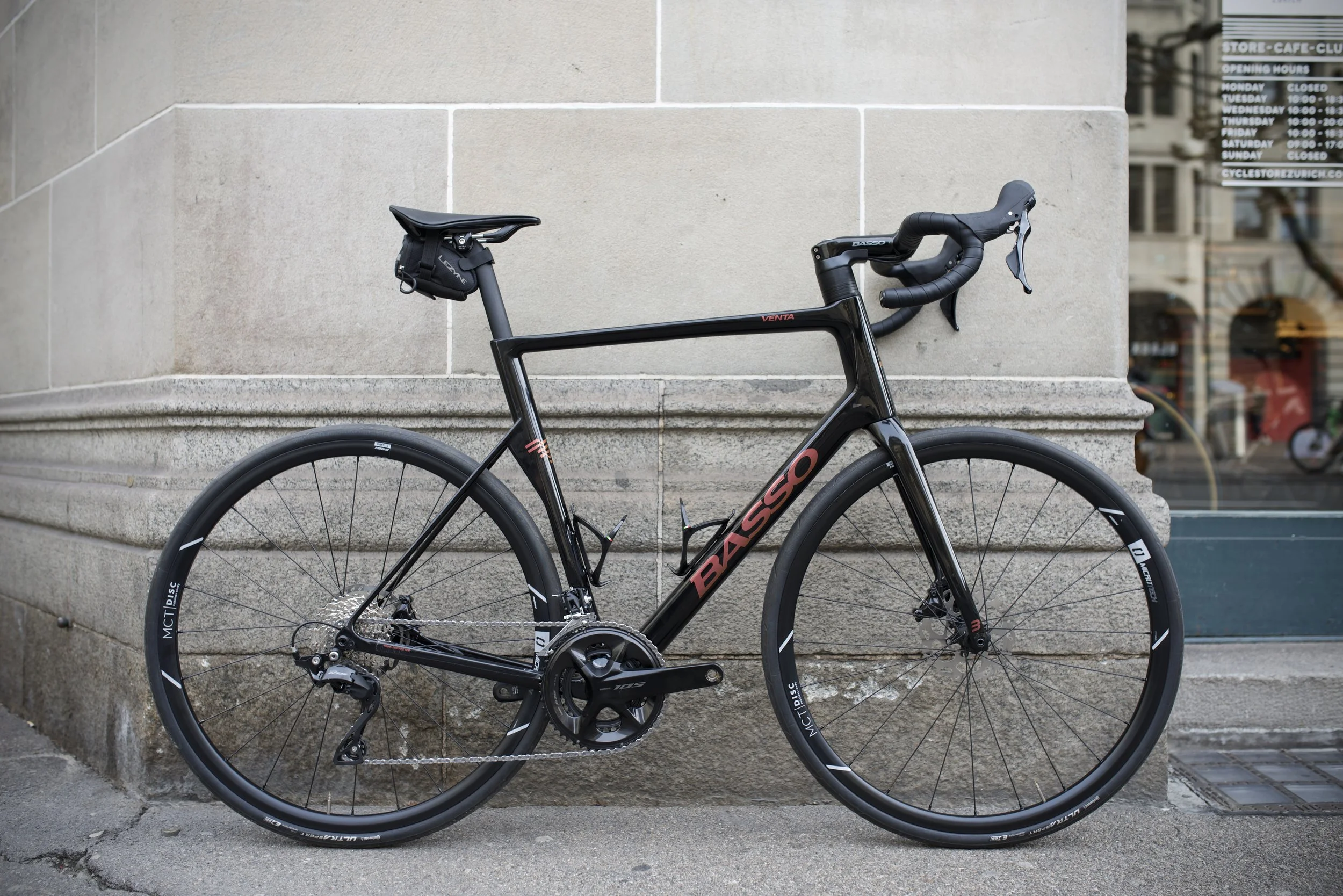 Black Basso gravel bike with drop handlebars and a water bottle holder, leaning against a stone building on a city sidewalk.