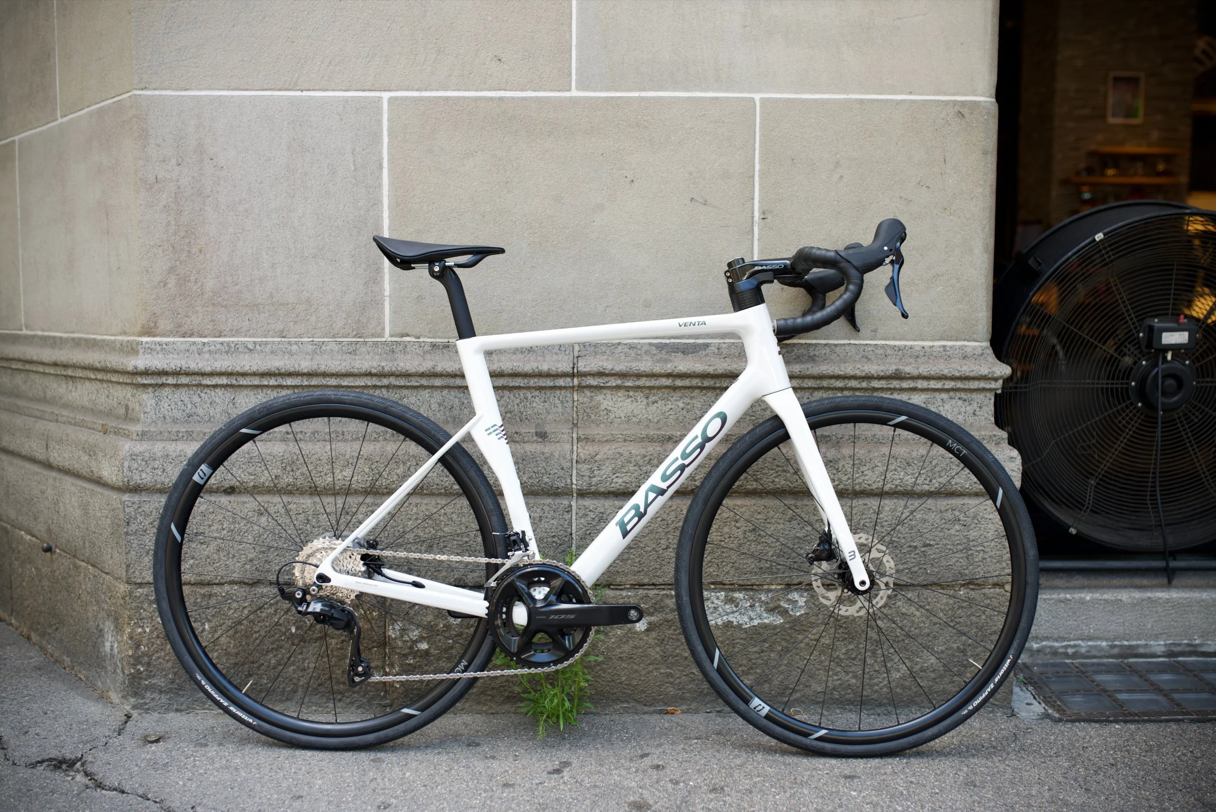 A modern gray and black road bicycle leaning against a stone wall exterior of a building.
