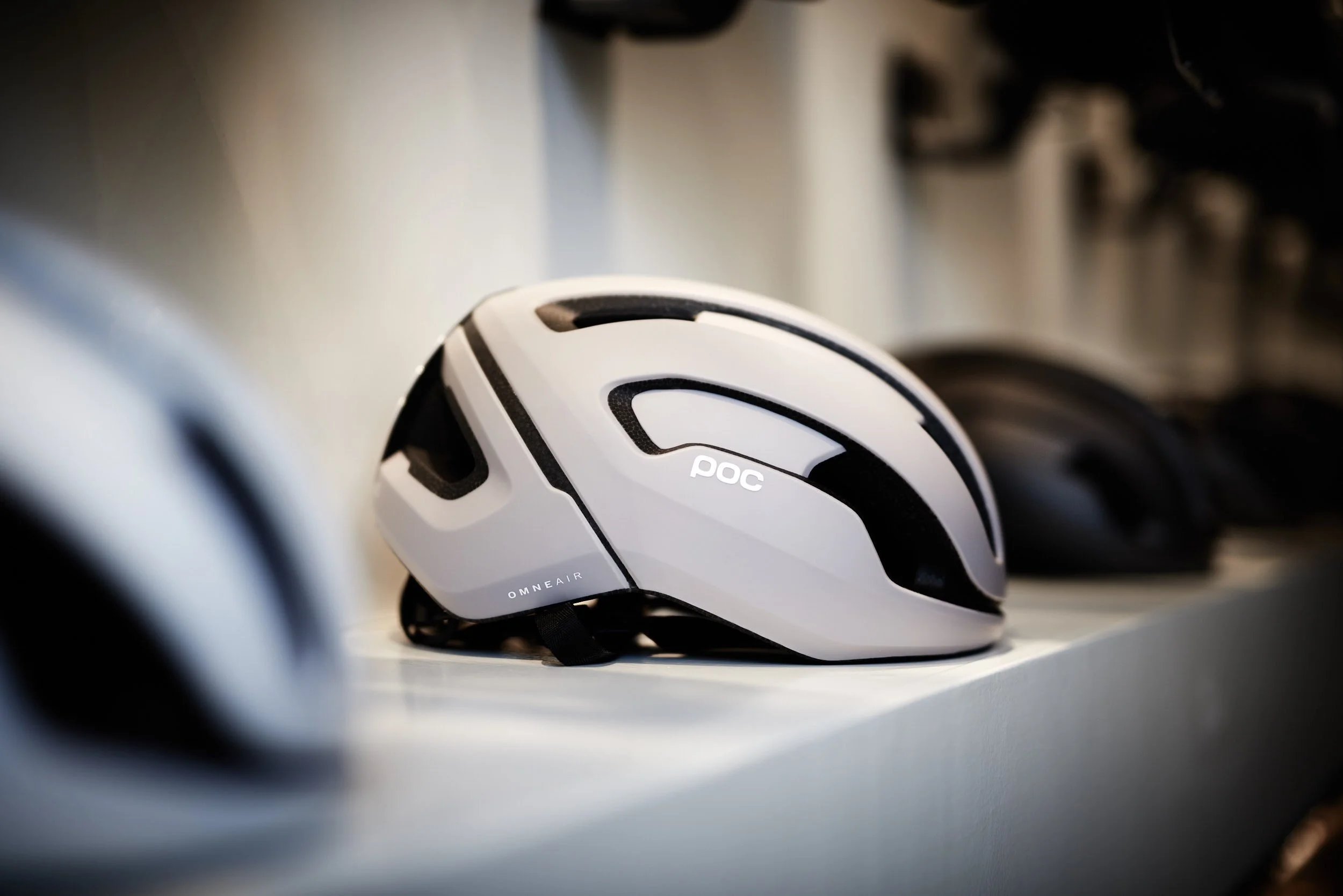 A white and black cycling helmet placed on a white shelf with other helmets in the background.