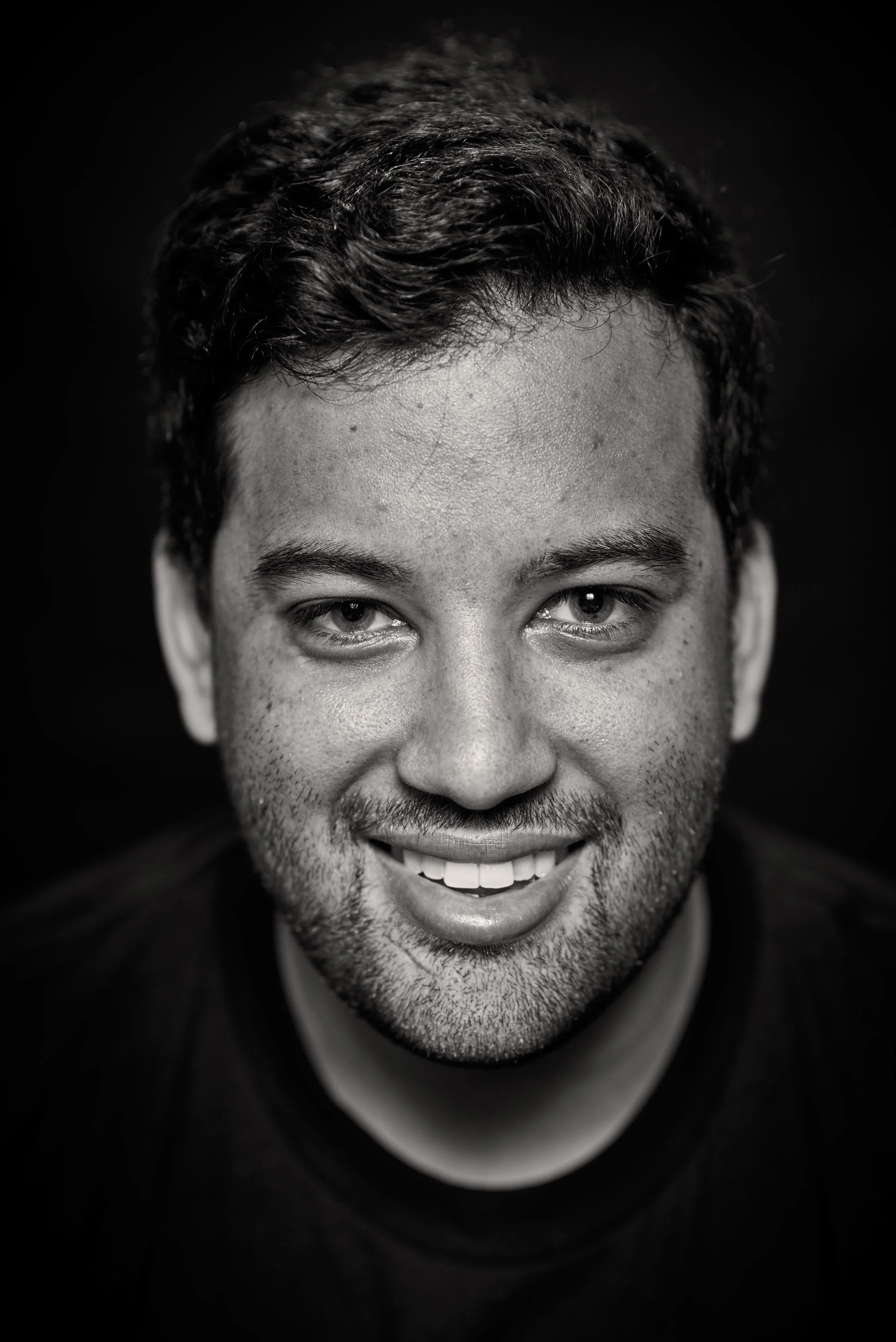 Black and white close-up portrait of smiling man with short, curly hair and slight beard.