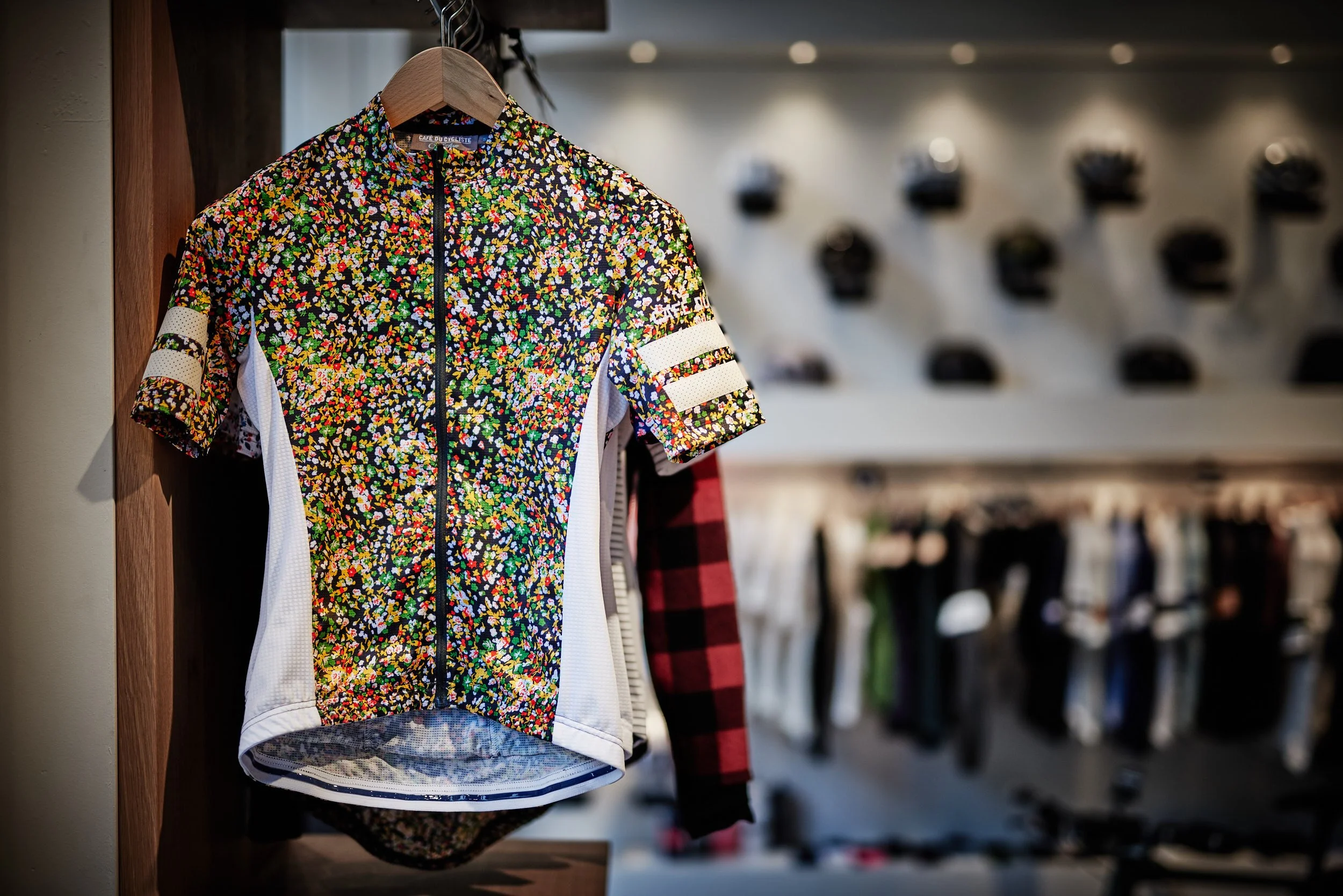 Colorful patterned cycling jersey hanging on a wooden rack in a retail store.
