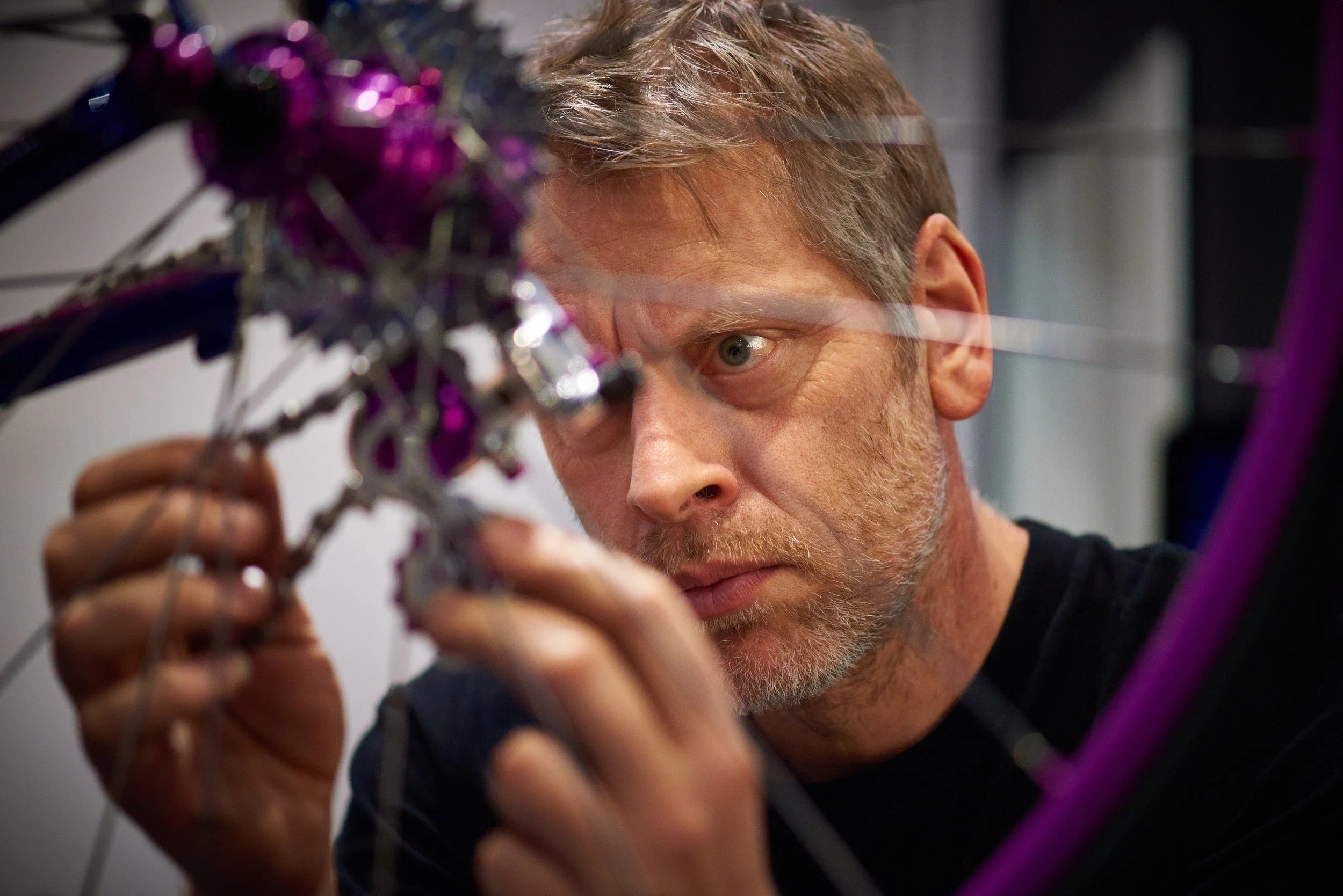 A man with gray hair and beard concentrating on repairing or assembling a bicycle, holding a part with both hands.