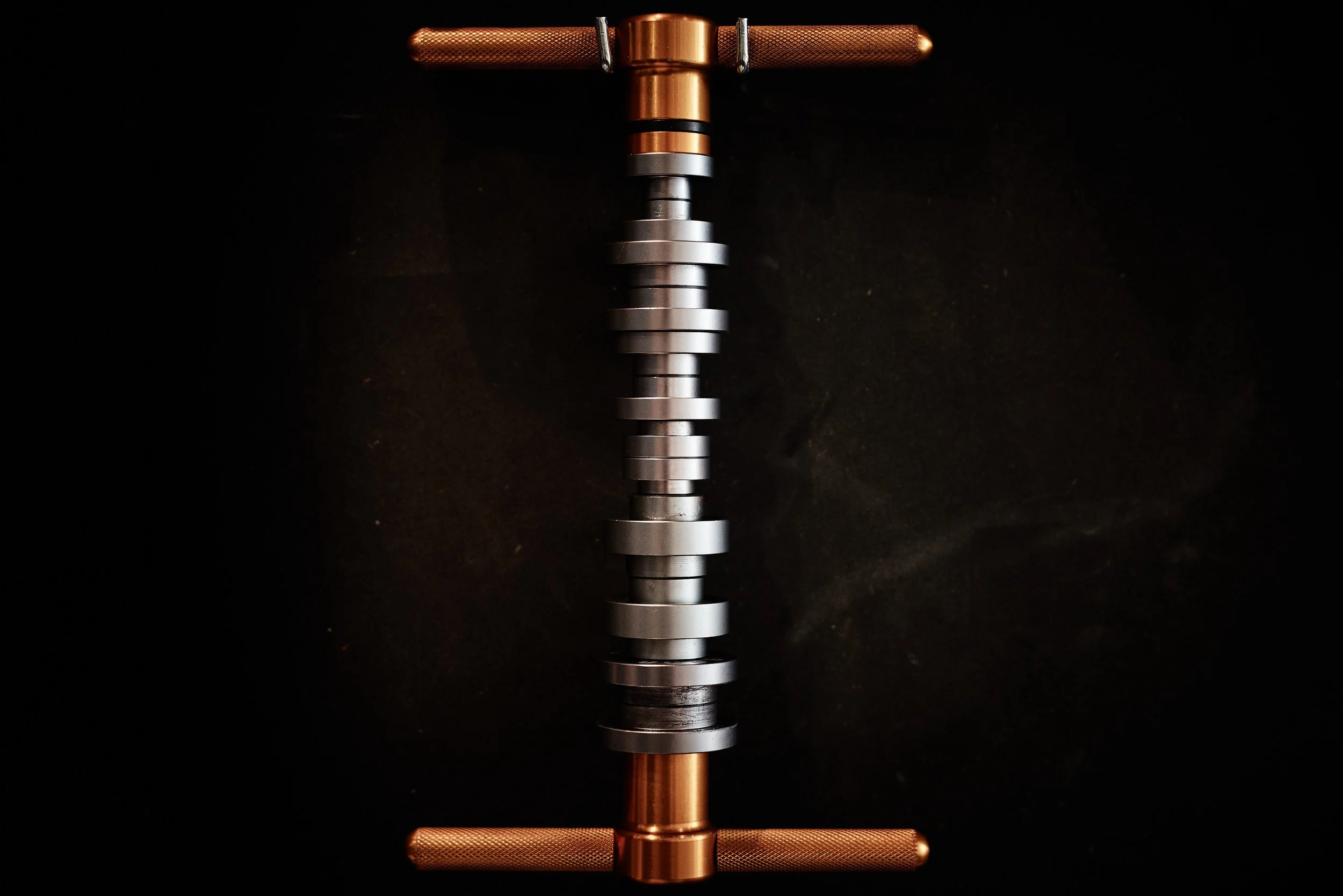 A metal camshaft with copper-colored gears at each end against a black background.