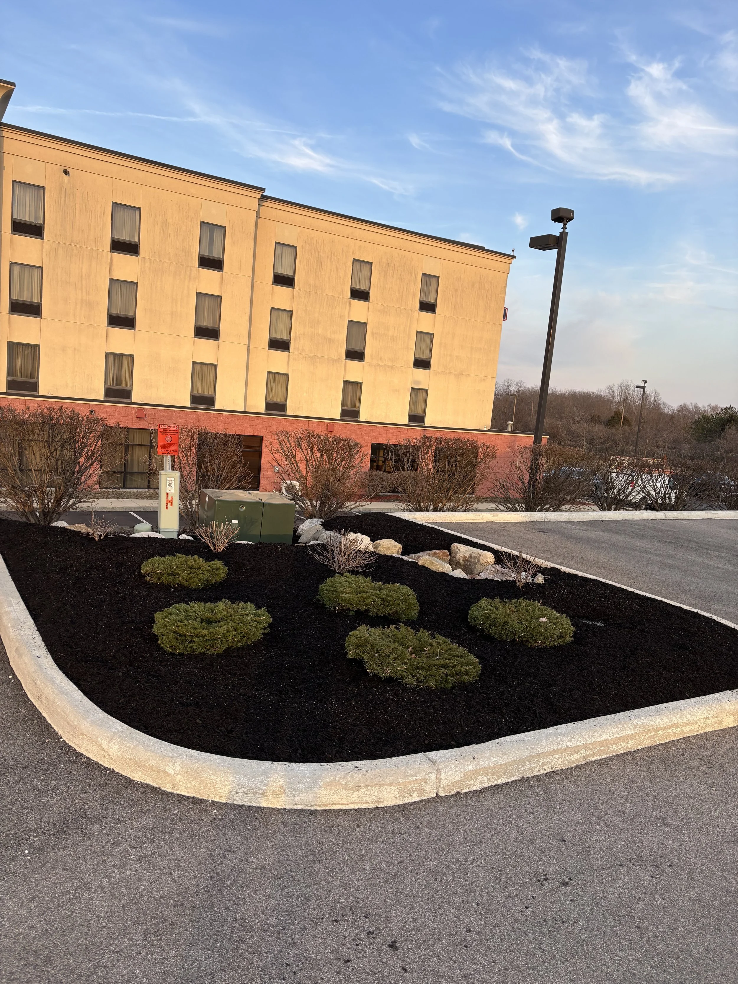 A landscaped parking lot island with small bushes and decorative rocks in front of a beige hotel building.