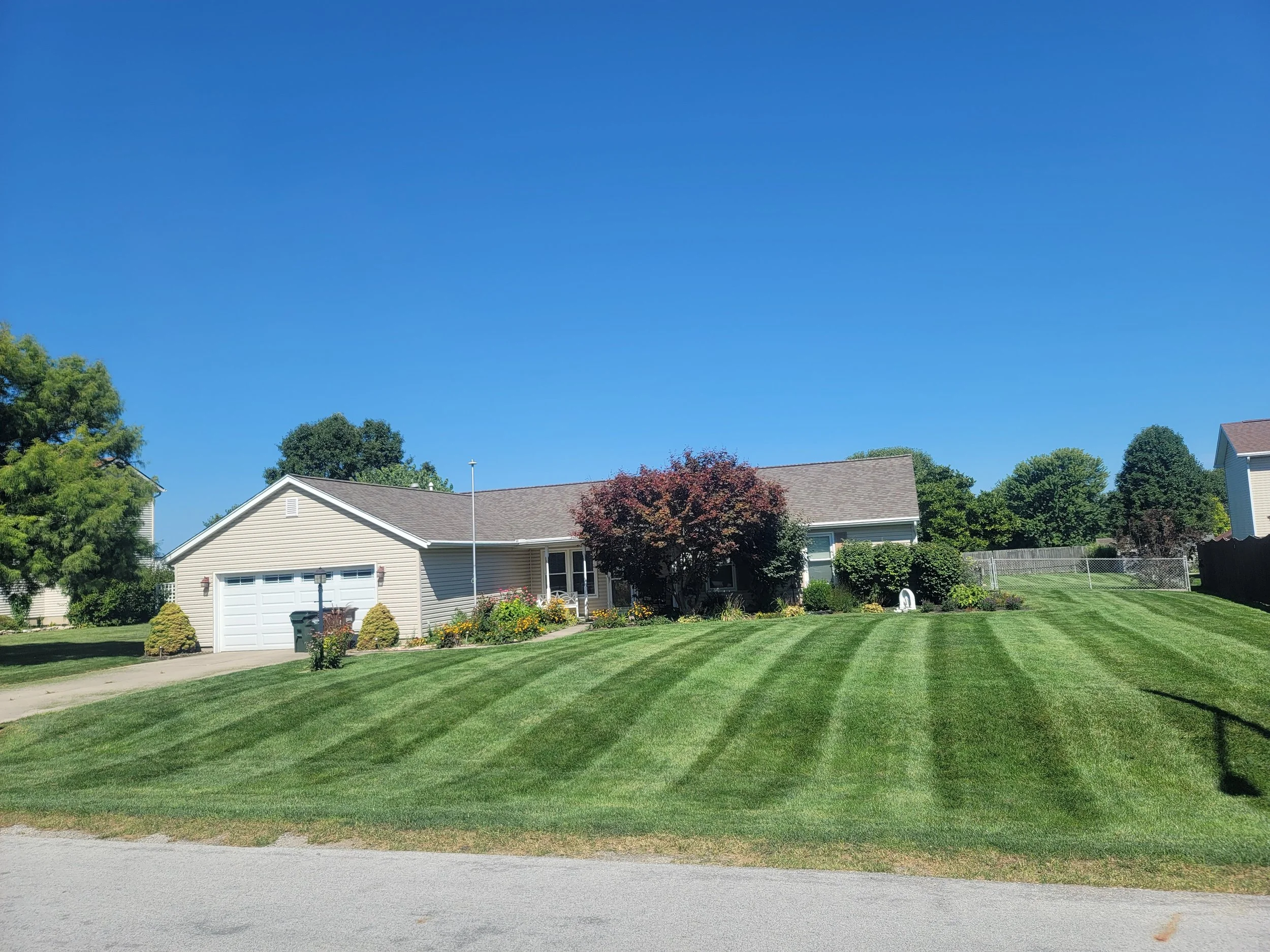 A suburban house with a well-kept lawn, a driveway, and trees under a clear blue sky.