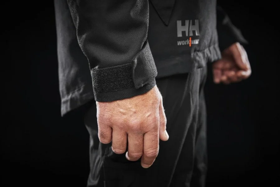 Main d'un homme vêtu d'une veste noire, poignets ajustés, dans un contexte sombre.