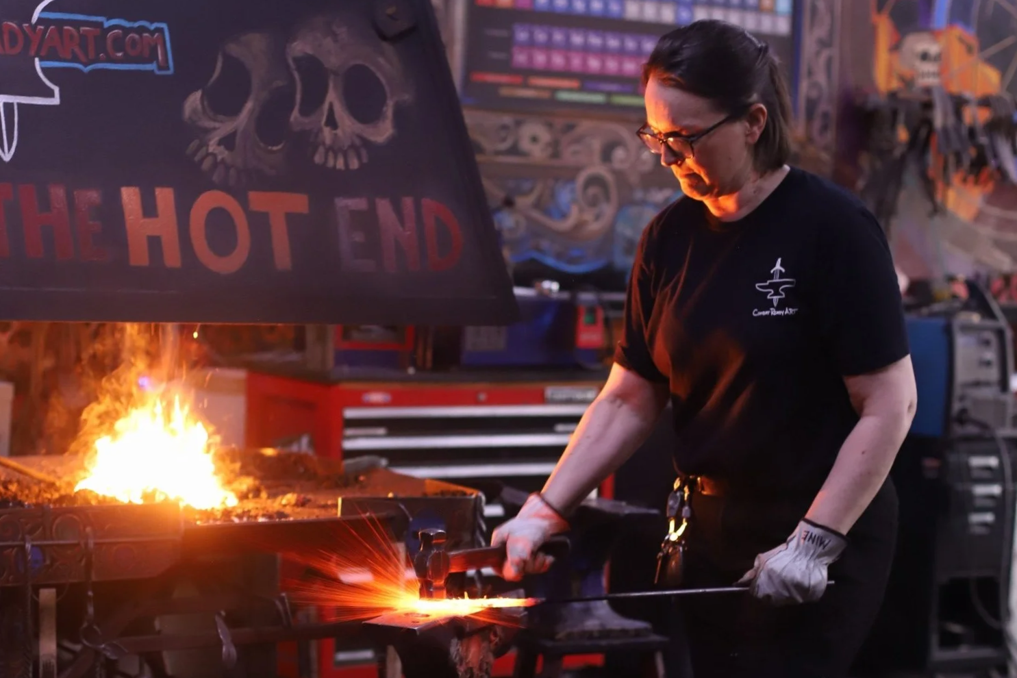 Blacksmith at Combat Ready Art forging glowing hot steel on an anvil, sparks flying