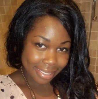 Smiling woman with long dark hair in a bathroom with tiled walls.