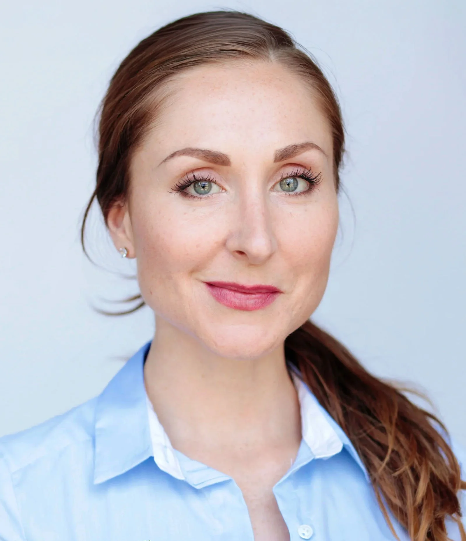 Woman with red hair, wearing a blue shirt, against a gray background.