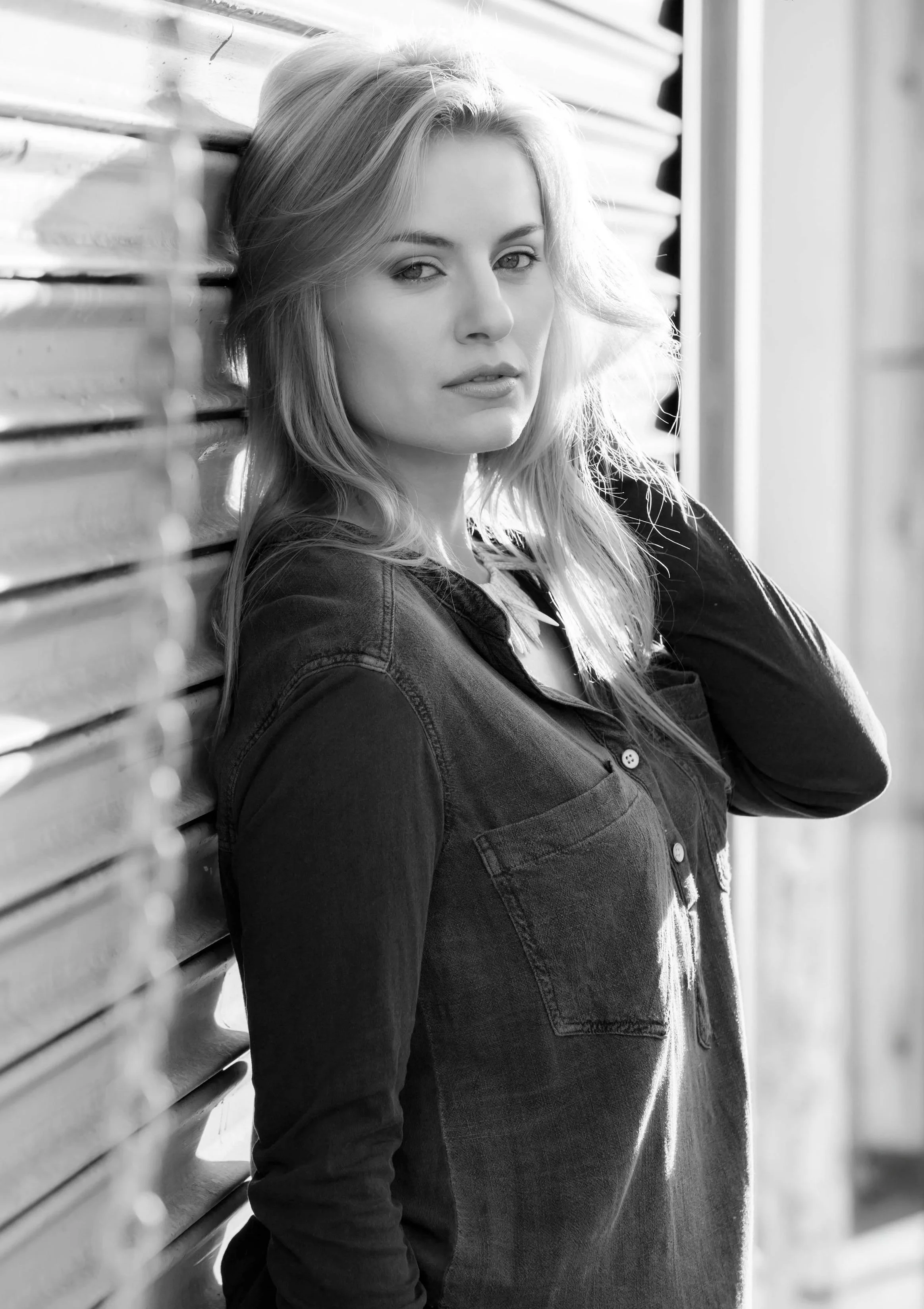 Black and white image of a woman with blonde hair wearing a denim shirt, standing outside