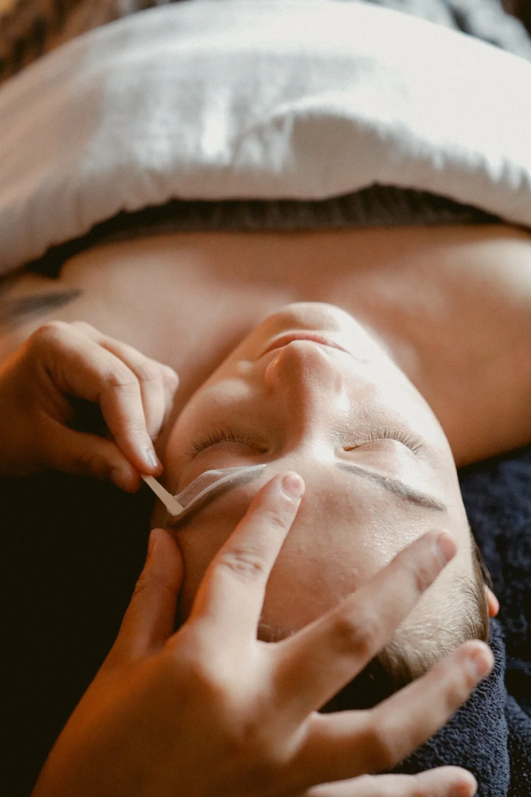A person is receiving a facial treatment, with a close-up of their face and hands applying a transparent facial mask or patch.