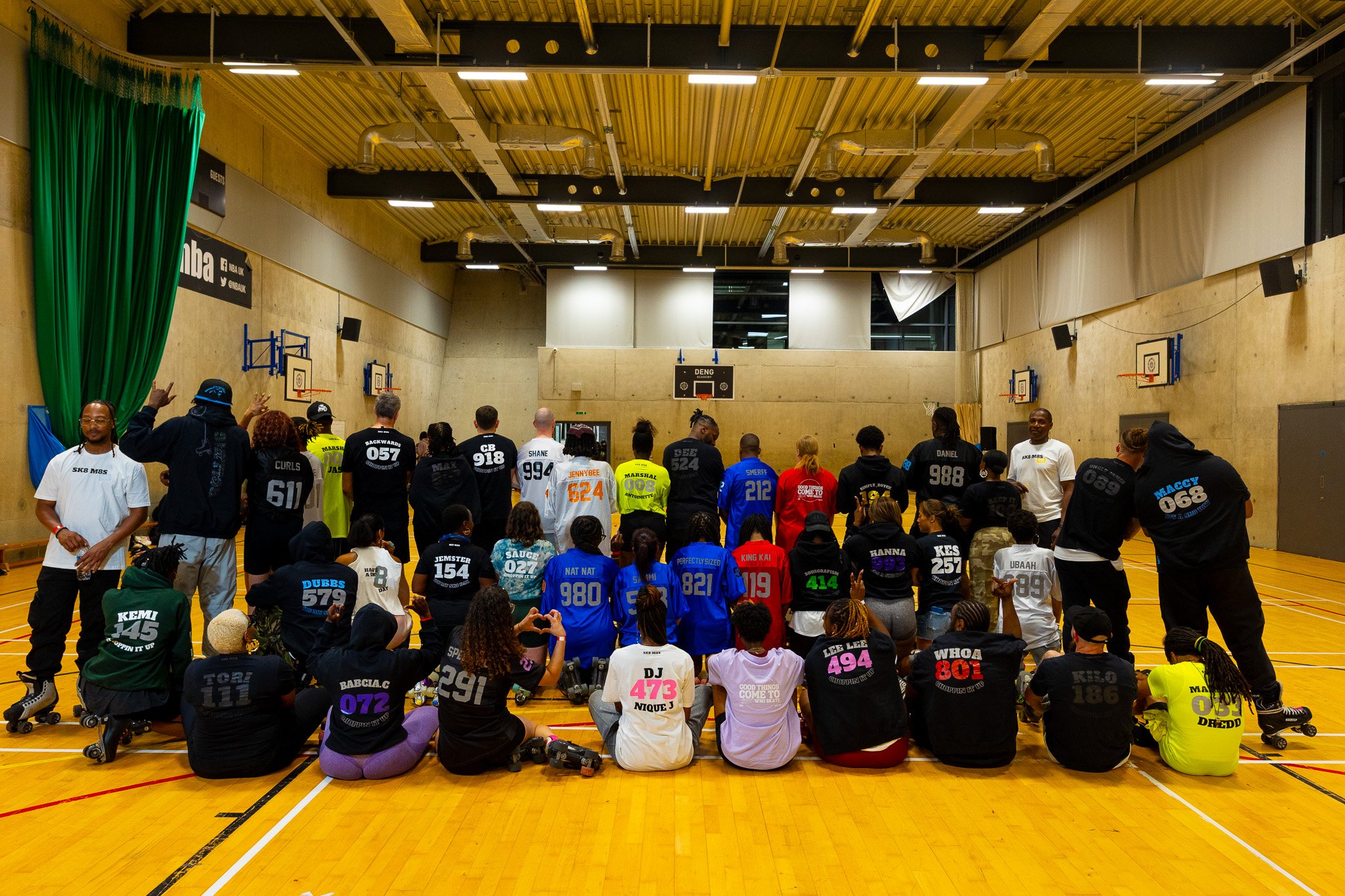 Group of skaters showing various personalised SK8 M8S numbers and names on their custom skate hoodies and custom skate jerseys, and limited drop clothing, gathered at a roller skating event. Image taken by photographer and roller skate India Mae Alby