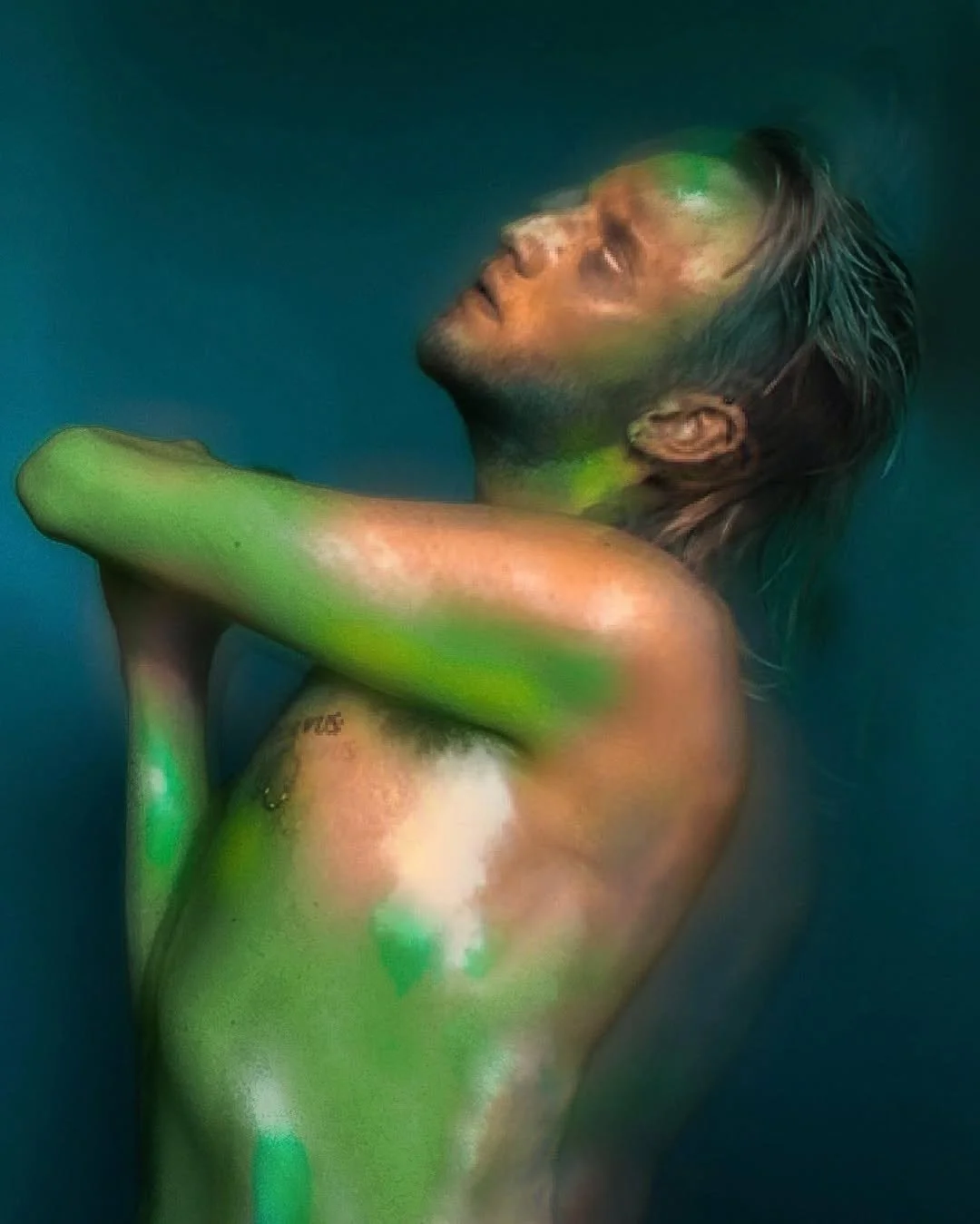 A person with closed eyes and slightly parted lips, submerged in water with green light reflections on their face and body, arms crossed over chest, with tousled short hair, and a tattoo on the side of their ribcage.