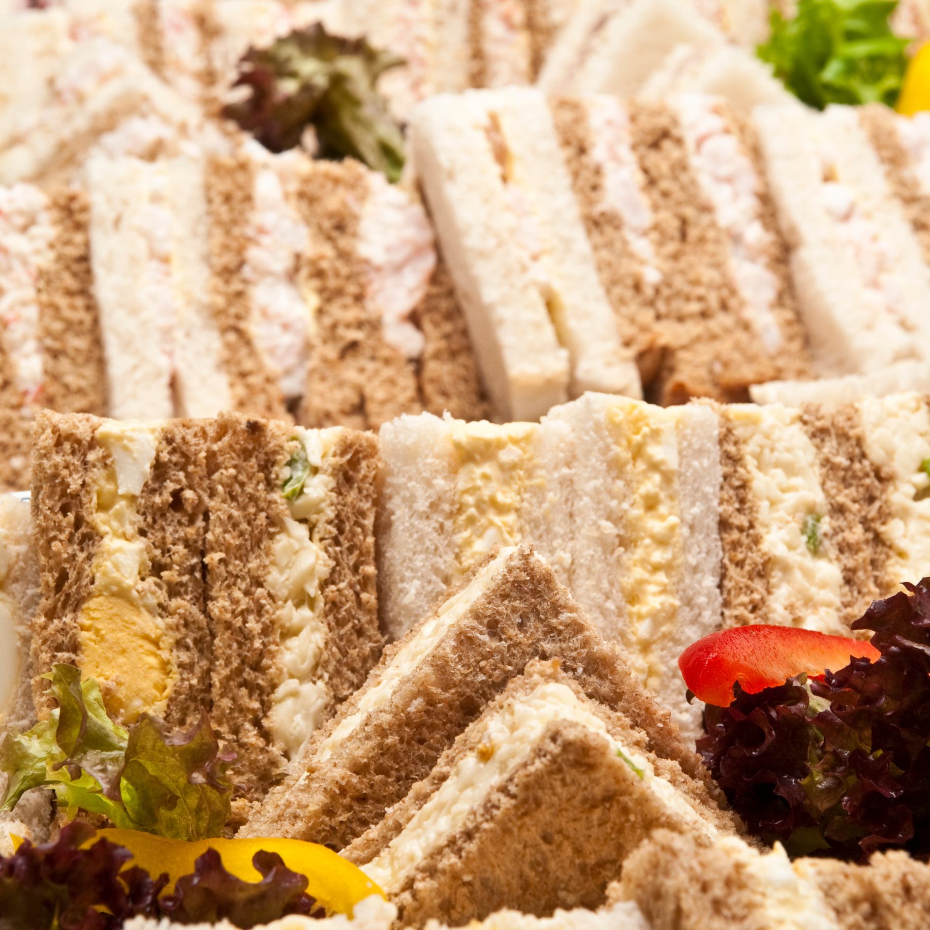 Close-up of assorted finger sandwiches with lettuce, tomato, and sliced vegetables, arranged on a platter.