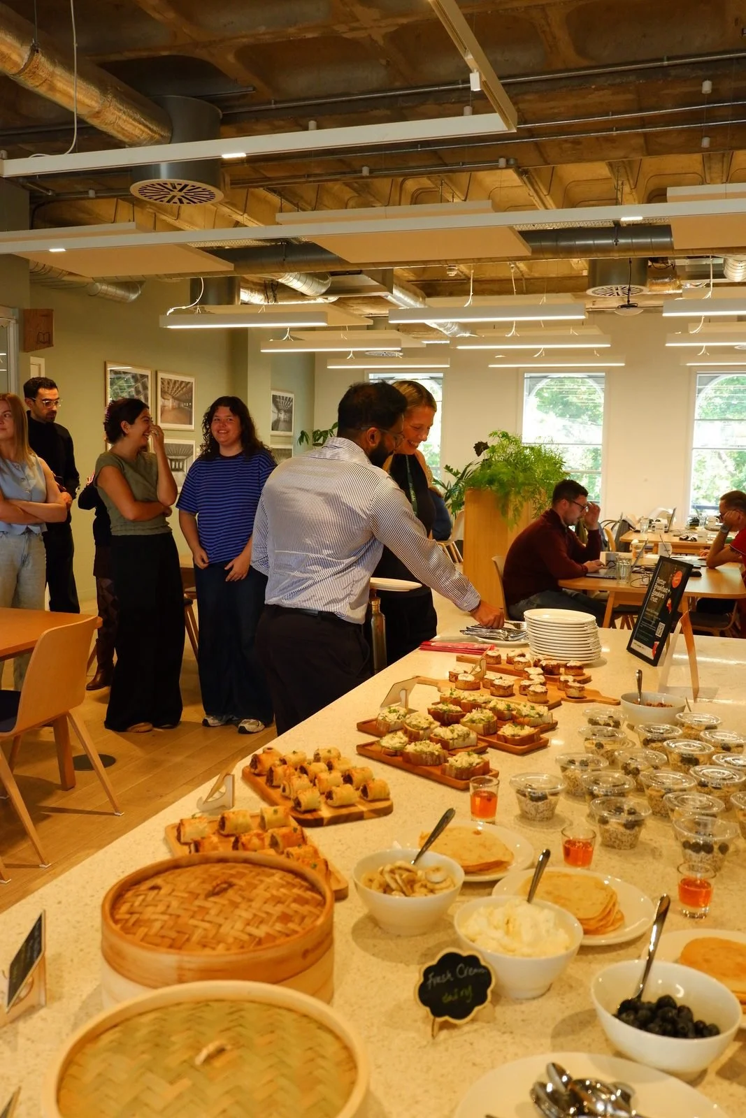 Colleagues serving themselves from a varied lunch buffet in a bright office