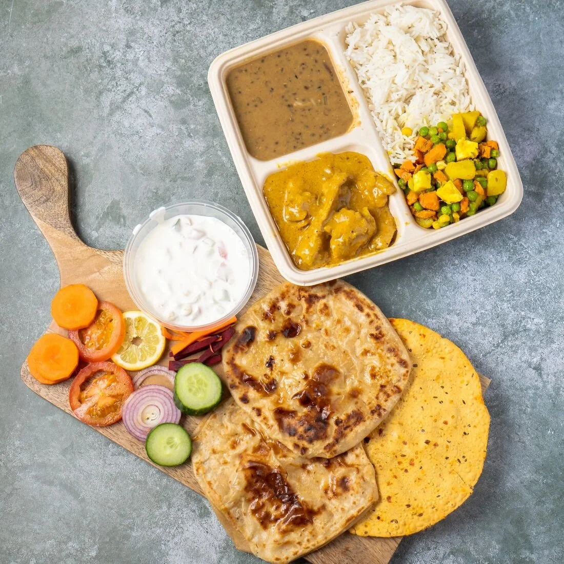 A packed lunch box with rice, curries and vegetables, served with flatbread and salad