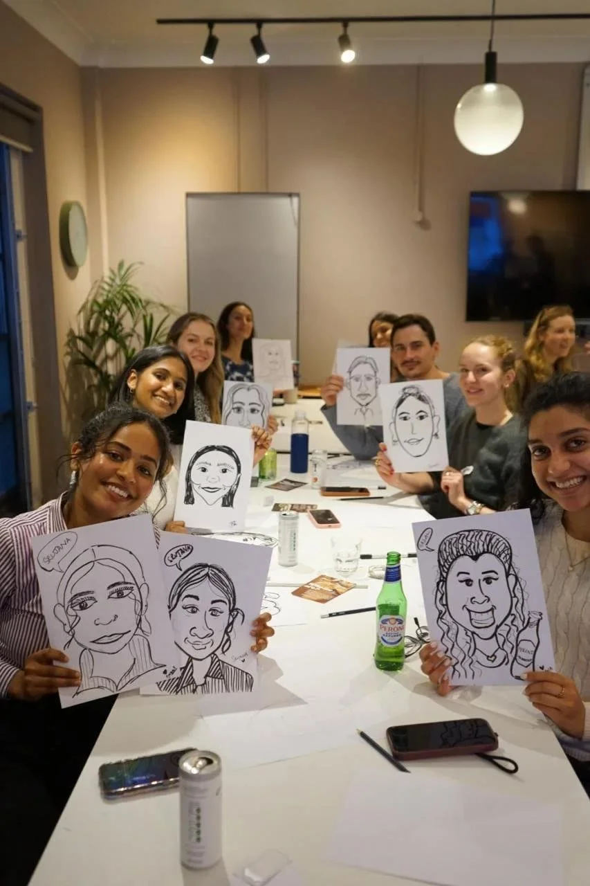A team holding up their finished drawings around a long table.