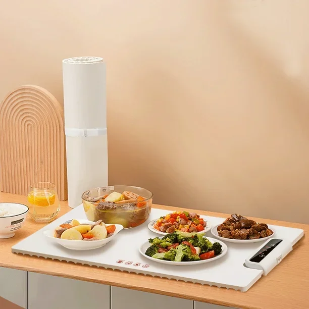 Mesa con comida en platos blancos, un recipiente con sopa, un vaso con jugo de naranja, y un paquete de comida para llevar en una mesa de madera, fondo con pared beige y decoración de madera.