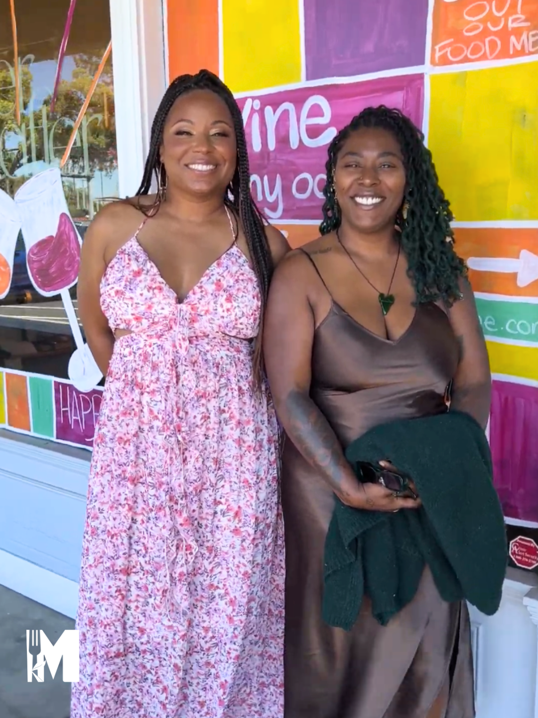 Two ladies posing in front of a colorful window in floral dresses