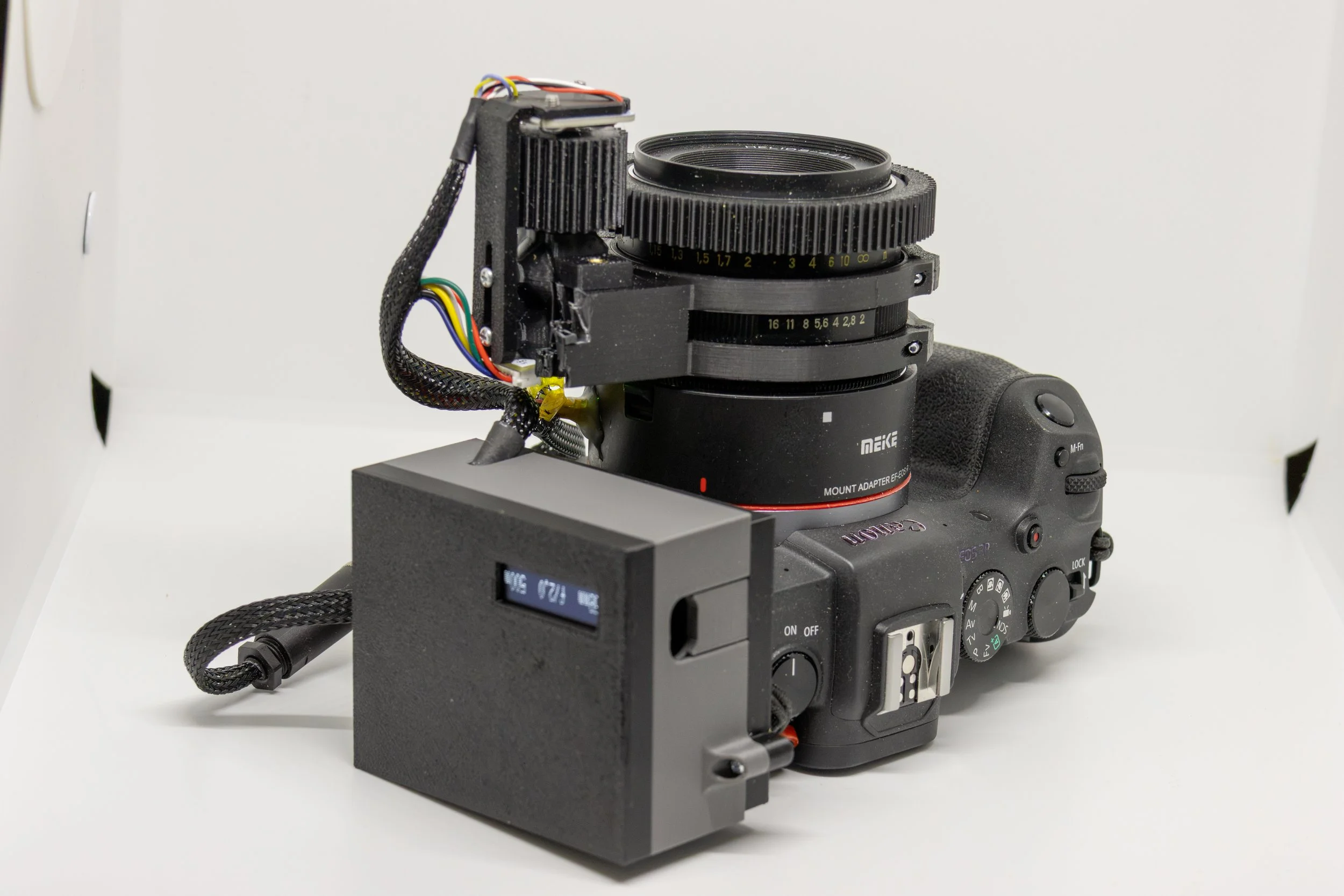 A camera with a mounted lens connected to a device via cables, placed on a black box against a plain white background.