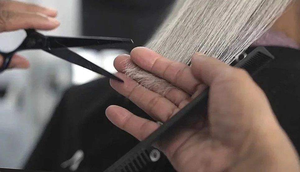 A person getting a haircut, with scissors in hand, while another person holds a mirror and shows the side of their head.